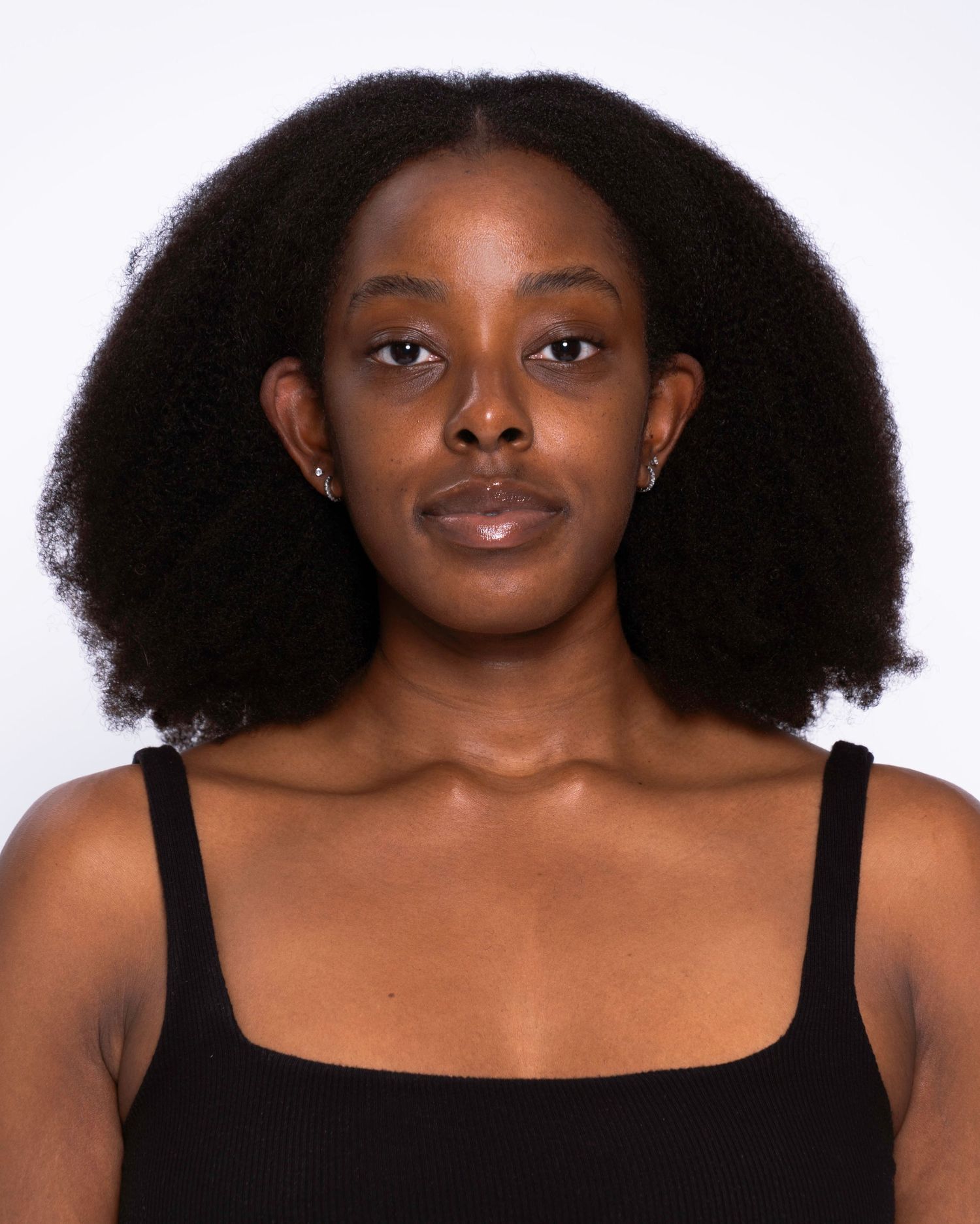 Young Black woman with natural afro hair wearing a black tank top, photographed against a white background.