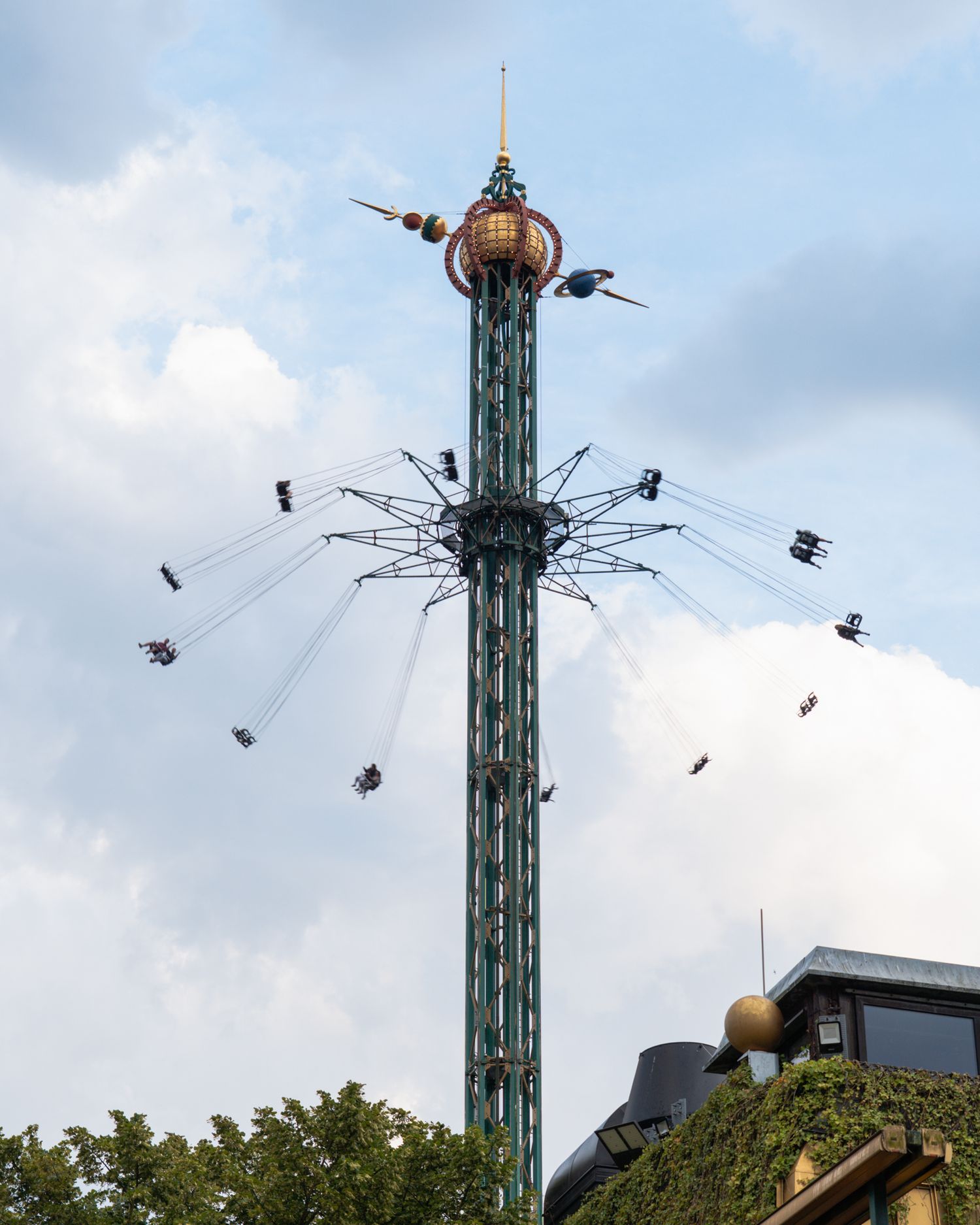 Amusement park swing ride spins against cloudy sky with multiple seats in motion.