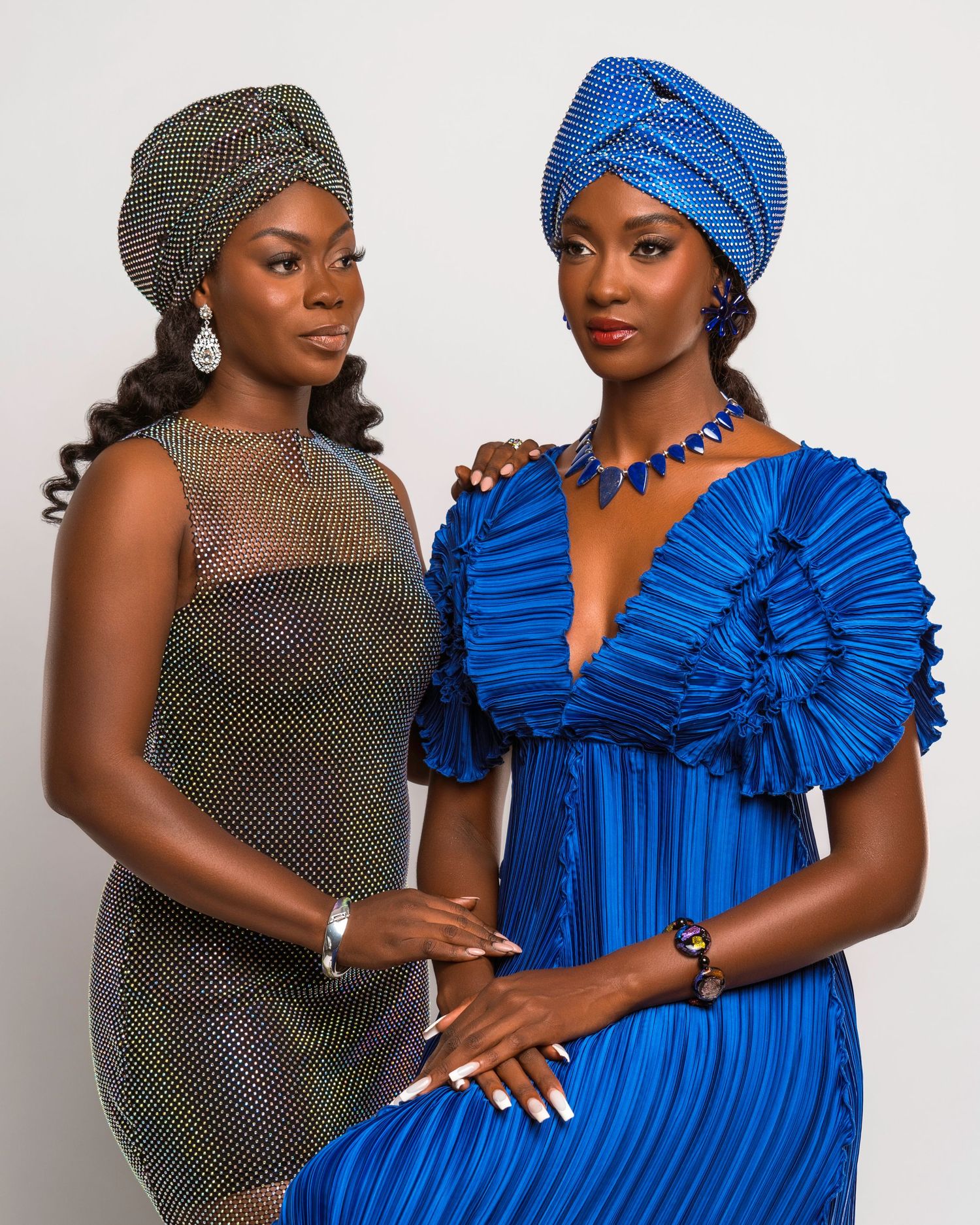 Two models posing in blue and metallic dresses with coordinated headwraps for fashion photoshoot.