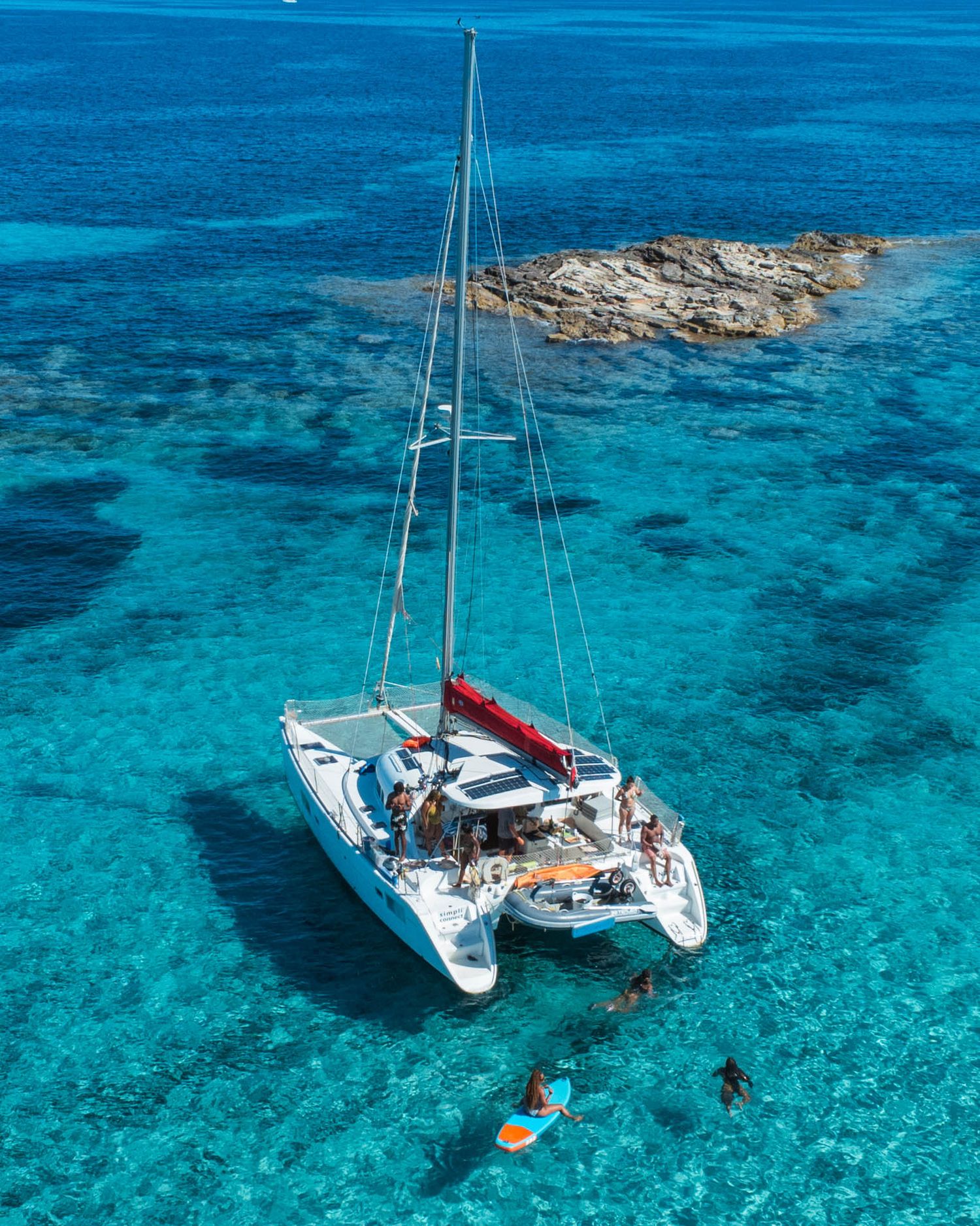 Catamaran yacht anchored in crystal clear turquoise waters near a coral reef.
