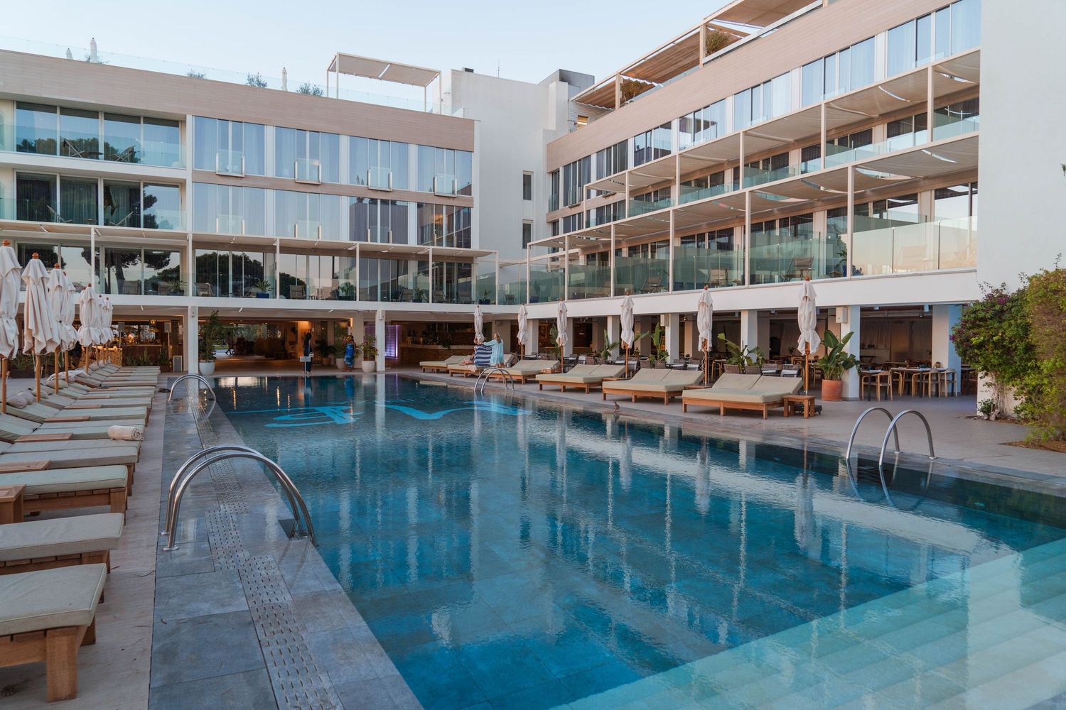 Modern resort hotel with long swimming pool and loungers at dusk.