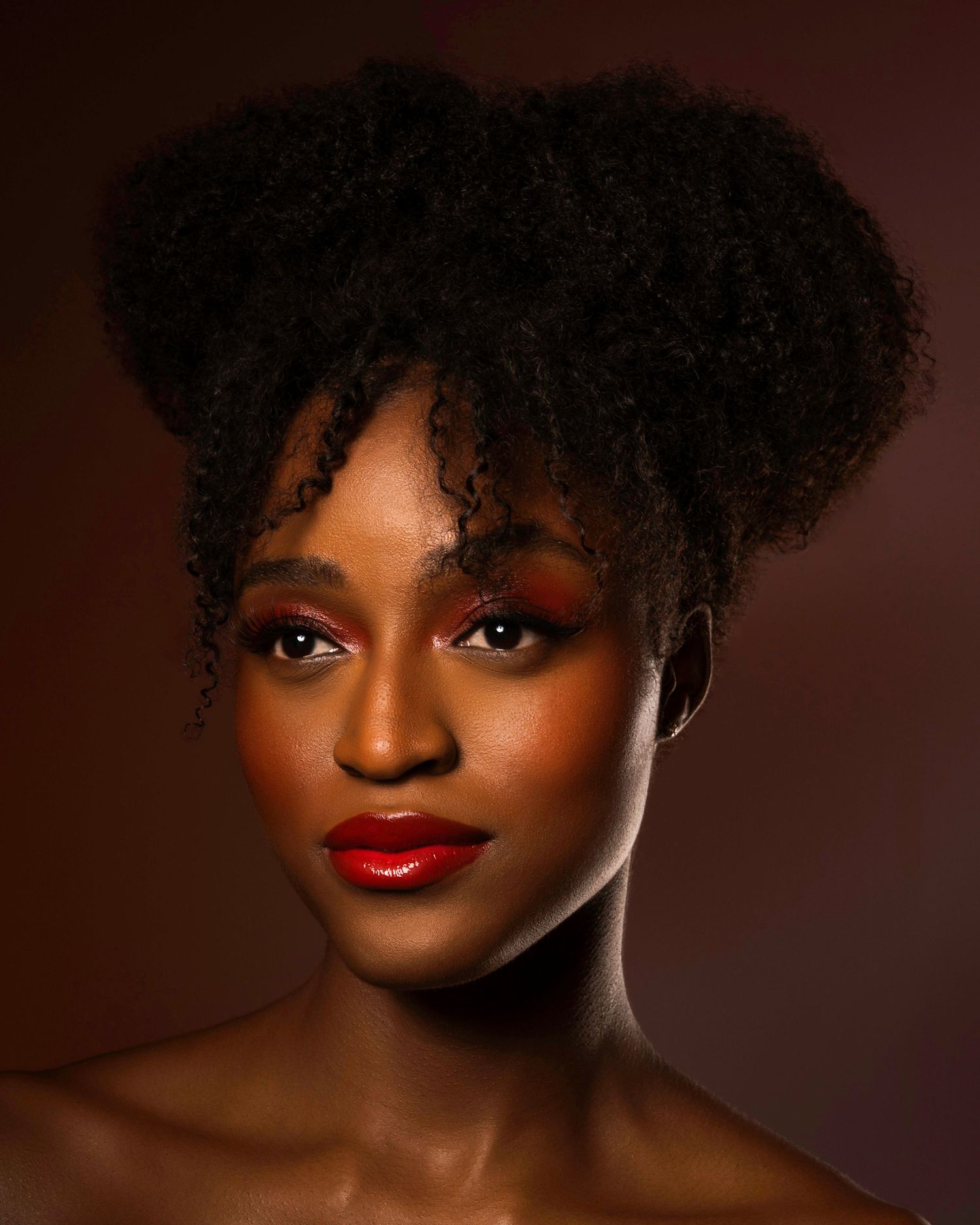 Dramatic beauty portrait with updo hairstyle and bold red lips against dark background.