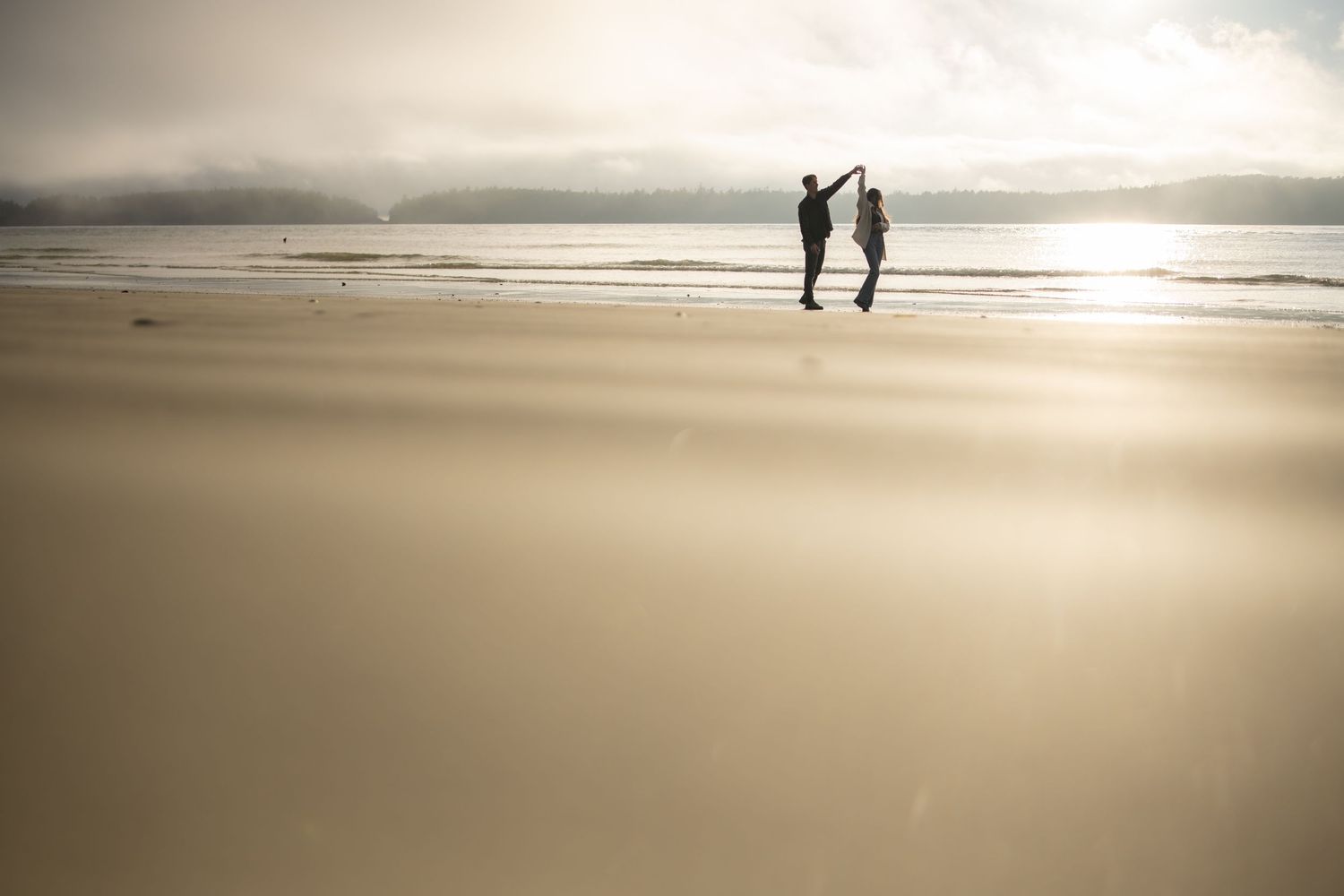 Silhouettes of couple holding hands on beach at golden sunset.