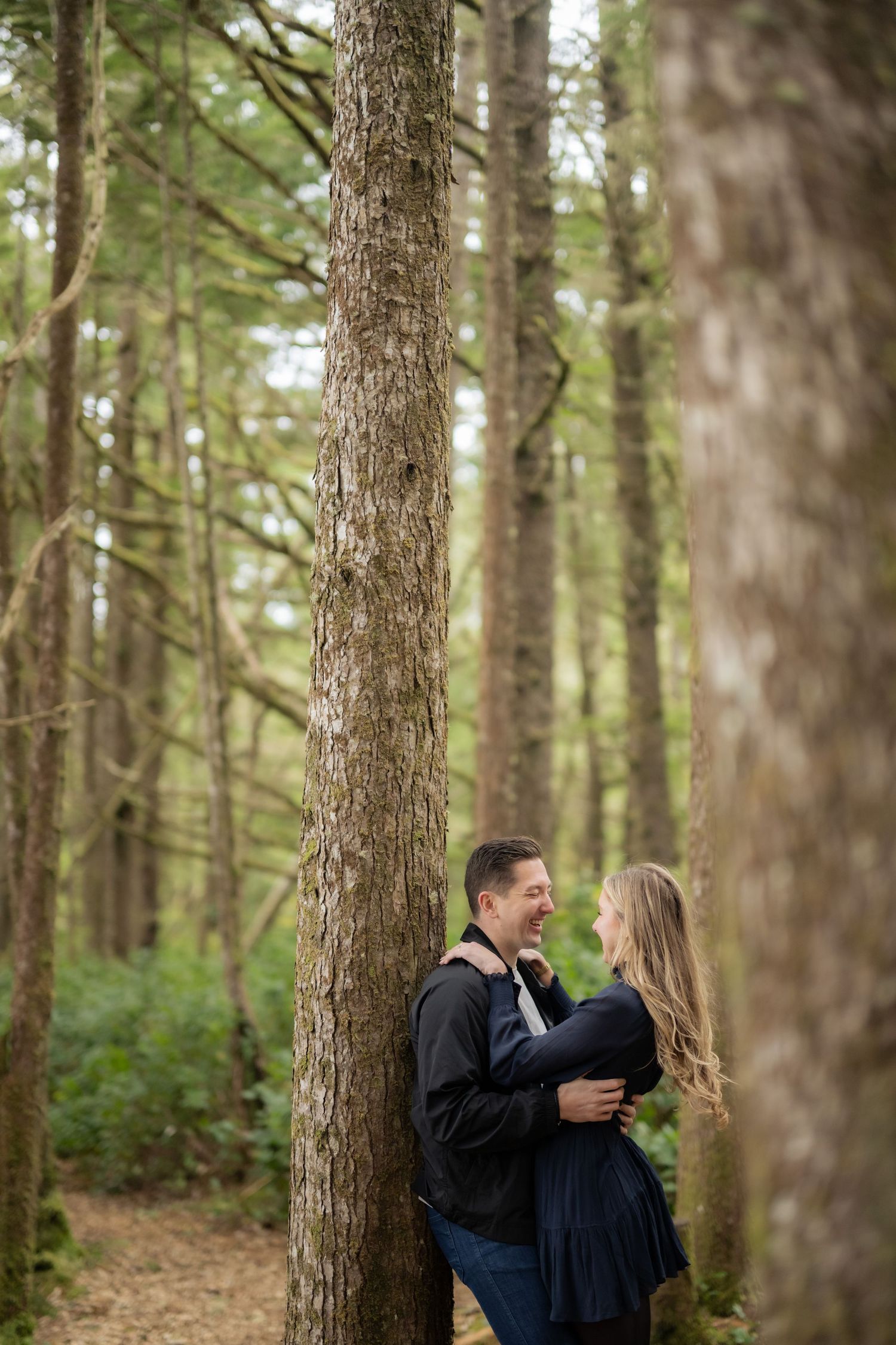A couple shares intimate moments among tall pine trees in a forest.