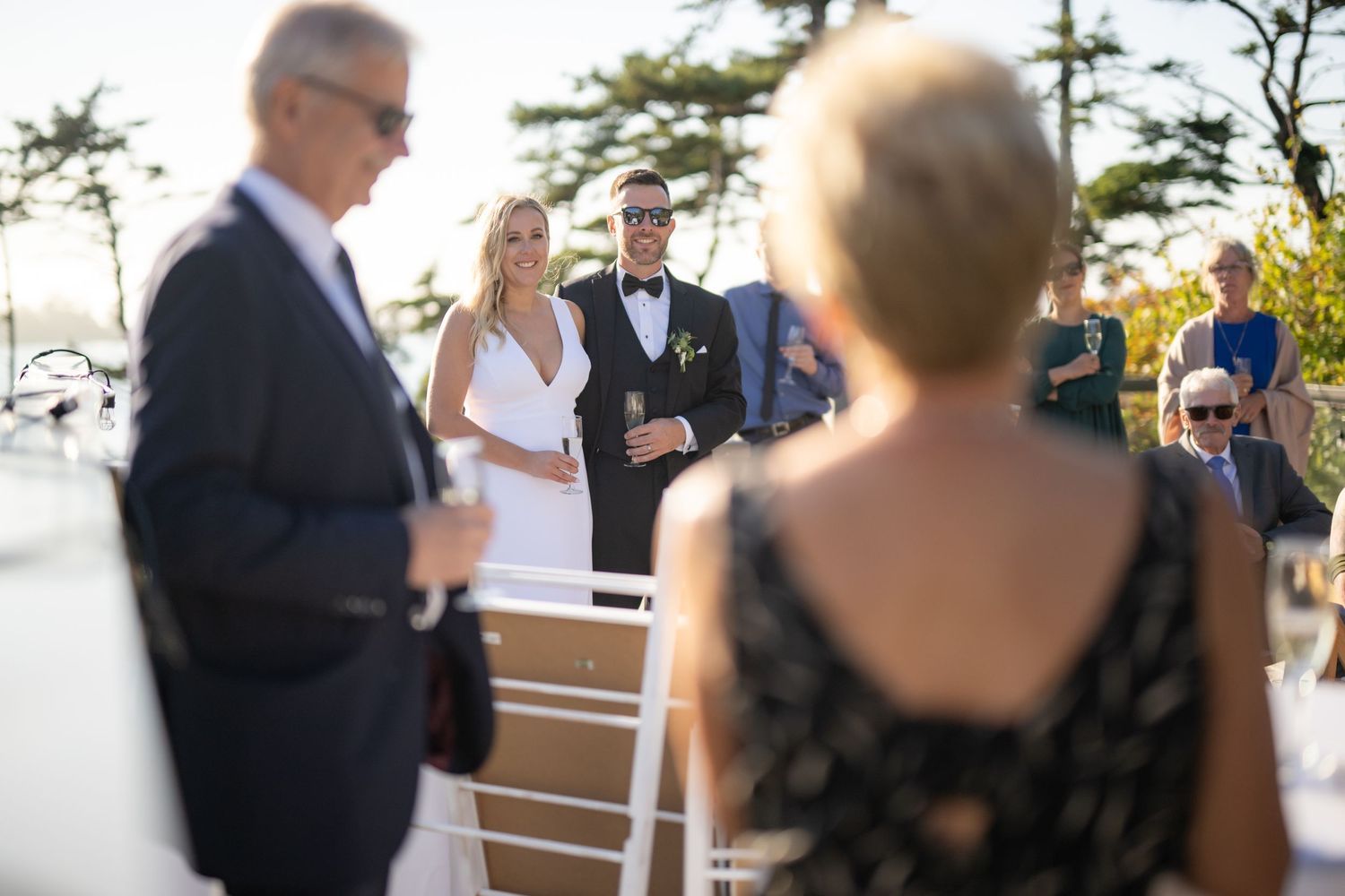Outdoor wedding ceremony on wooden deck with ocean and pine trees in background.