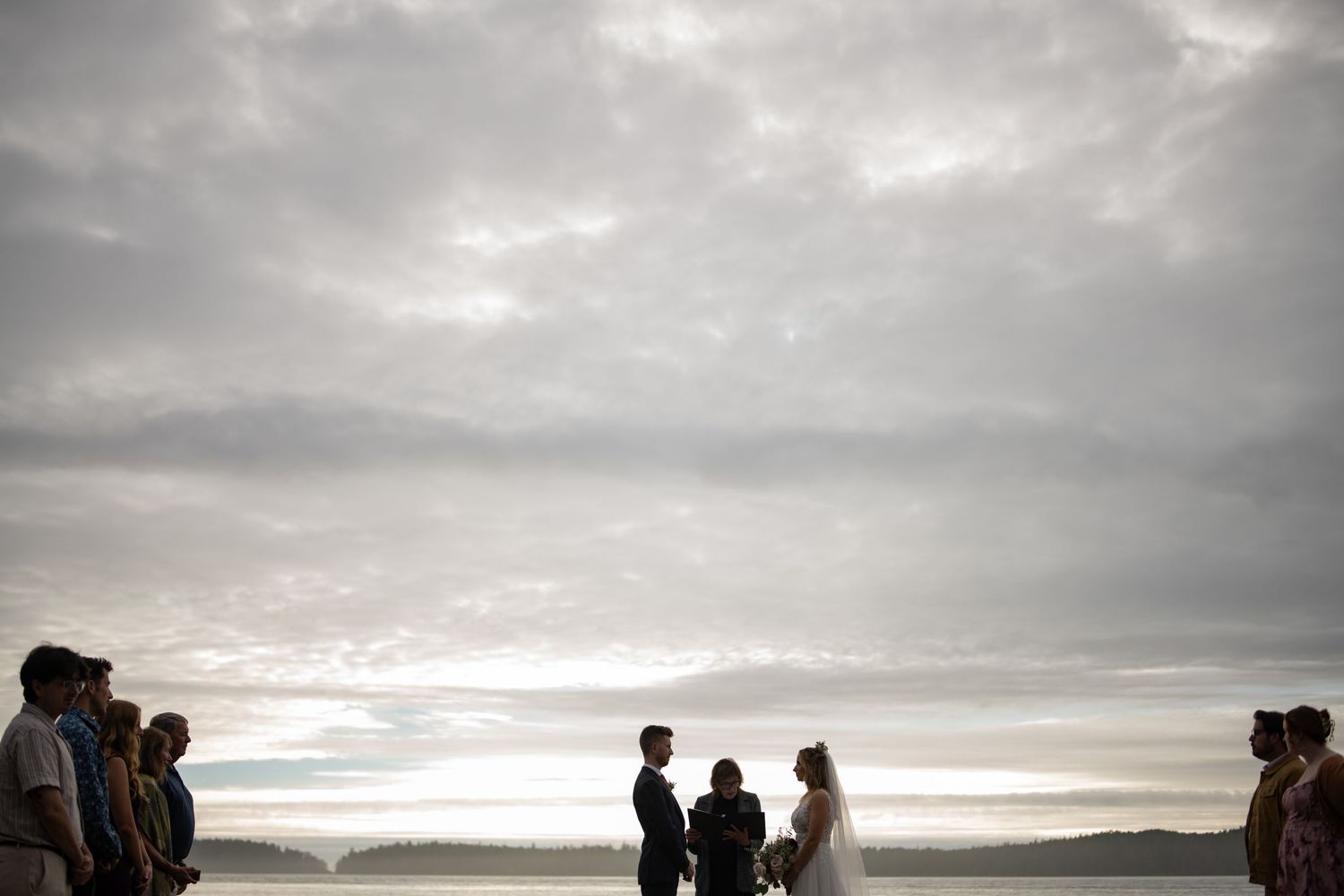 Moody beach wedding ceremony setup with dramatic cloudy skies over the ocean.