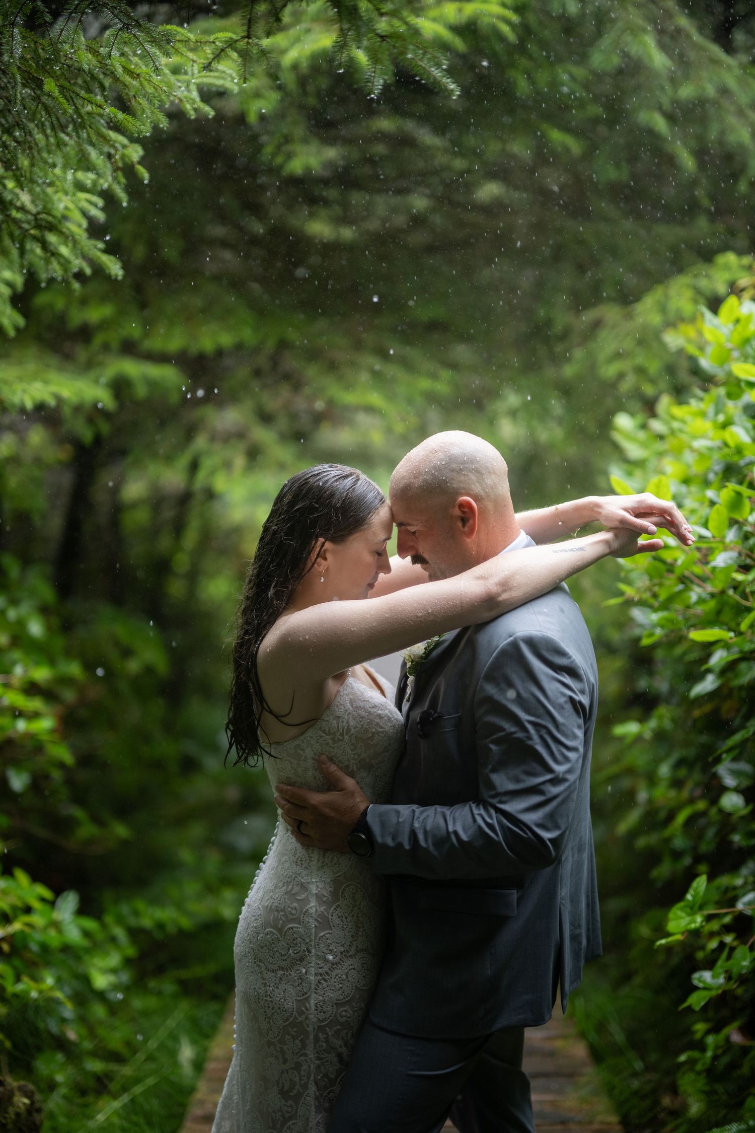 Couple shares a romantic dance moment in a rainy forest setting.