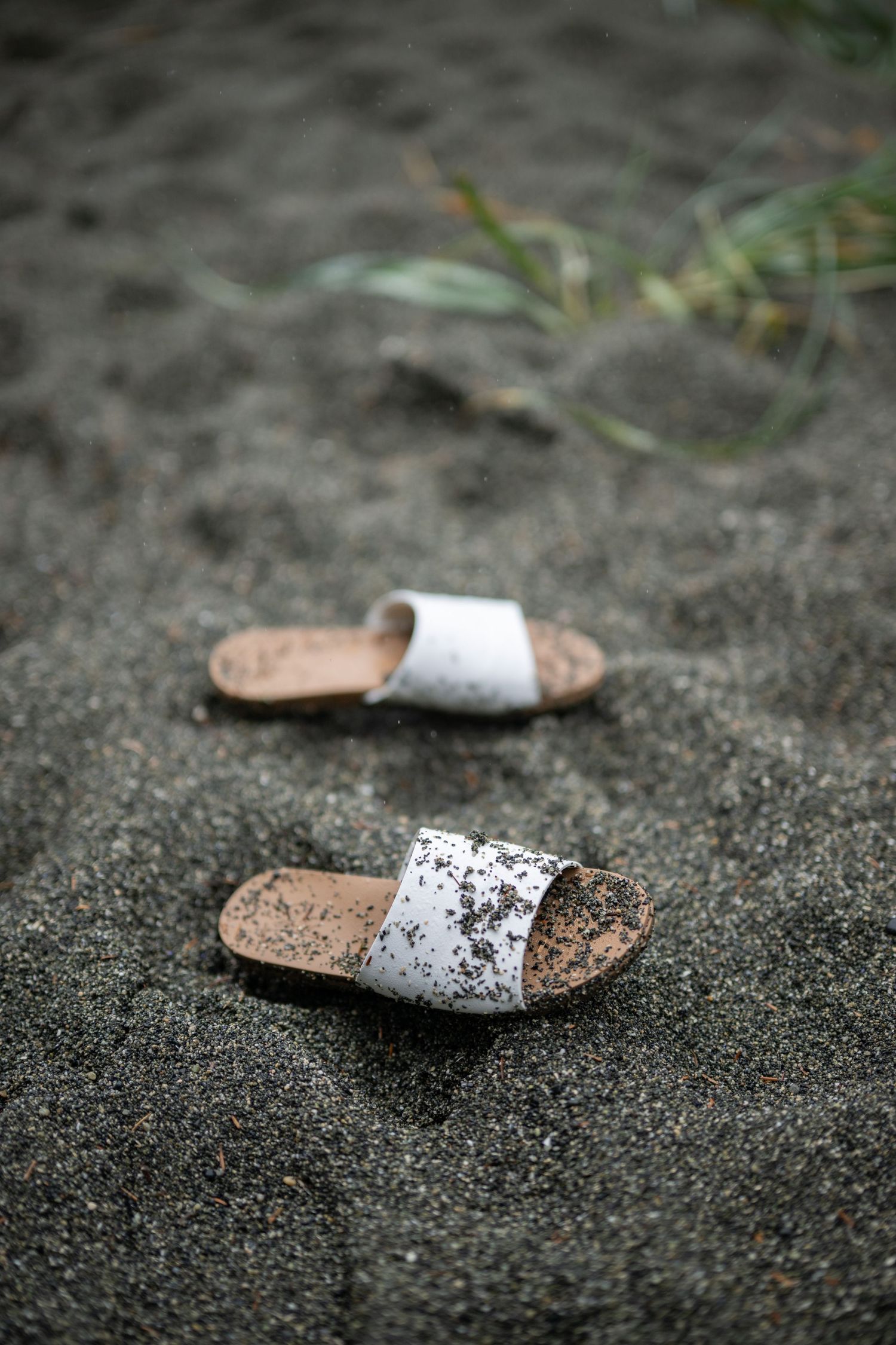 Two white sparkly sandals sit abandoned on dark volcanic sand.