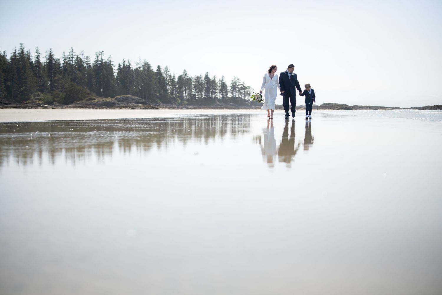 Small figures cast long reflections on vast empty beach landscape.