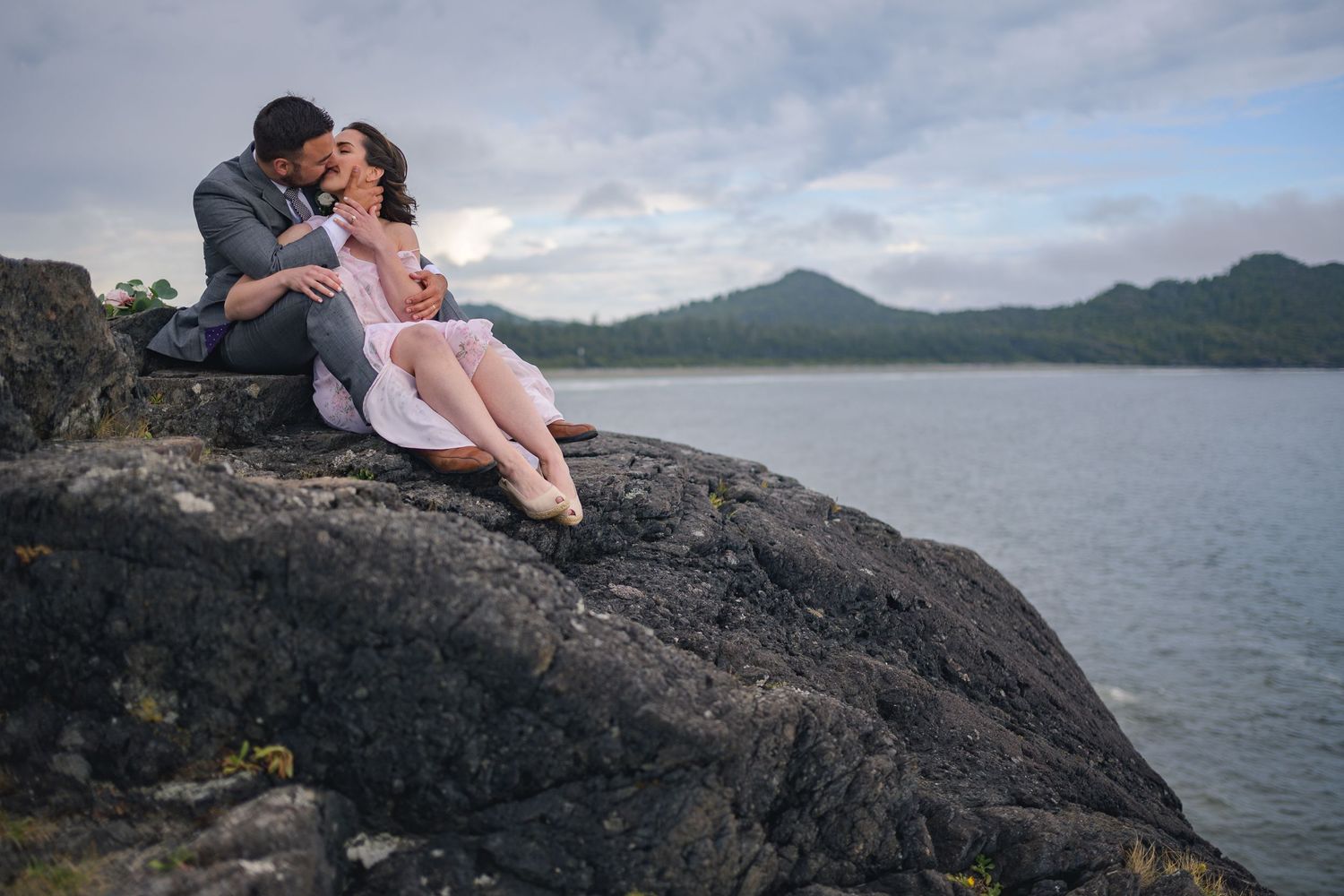 Romantic couple embraces on rocky coastal cliffs overlooking the ocean at sunset.