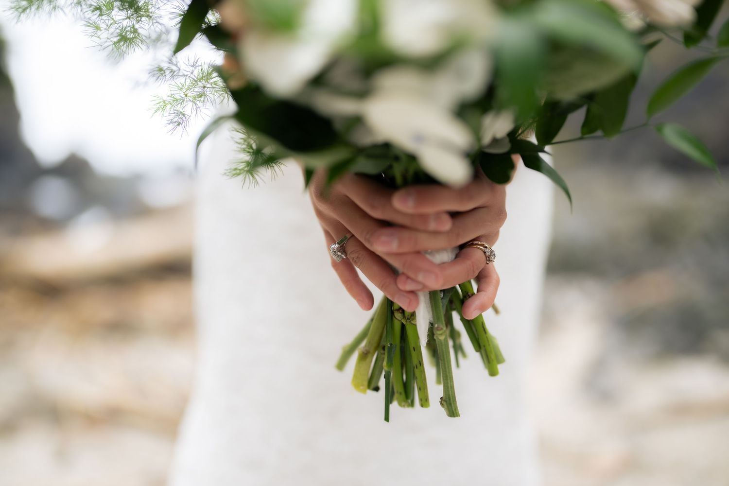 Close-up of white and green wedding bouquet held against coastal background.