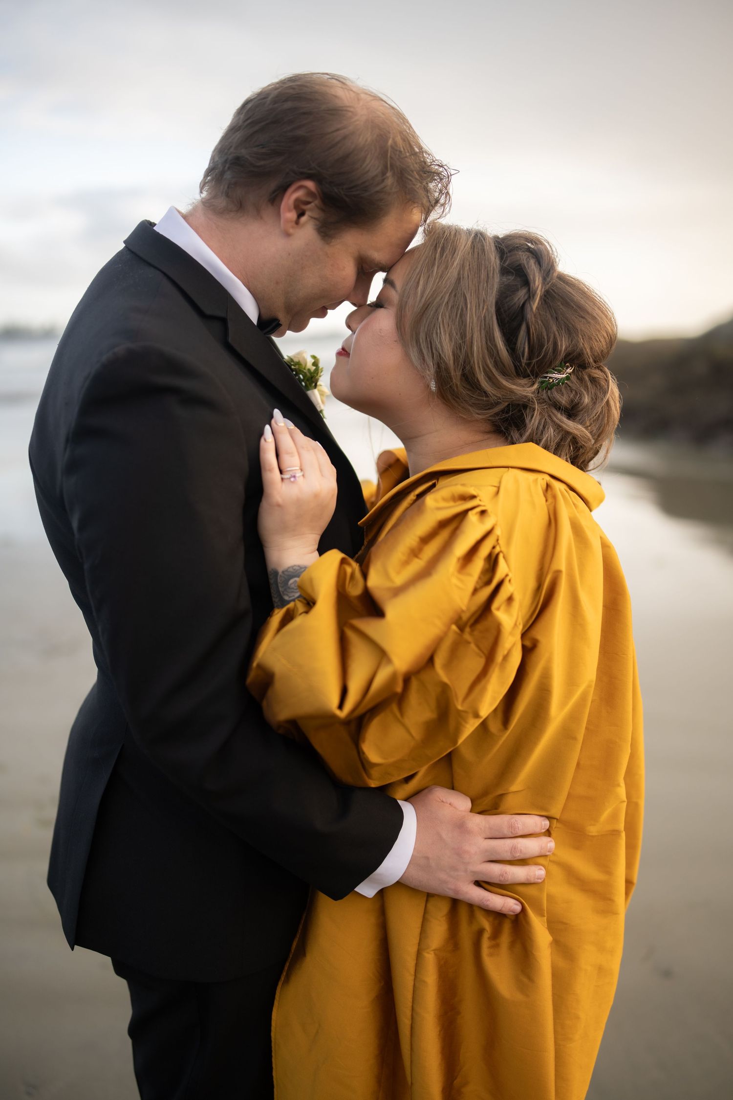 A romantic moment shared on a moody beach with one person in yellow and another in black.