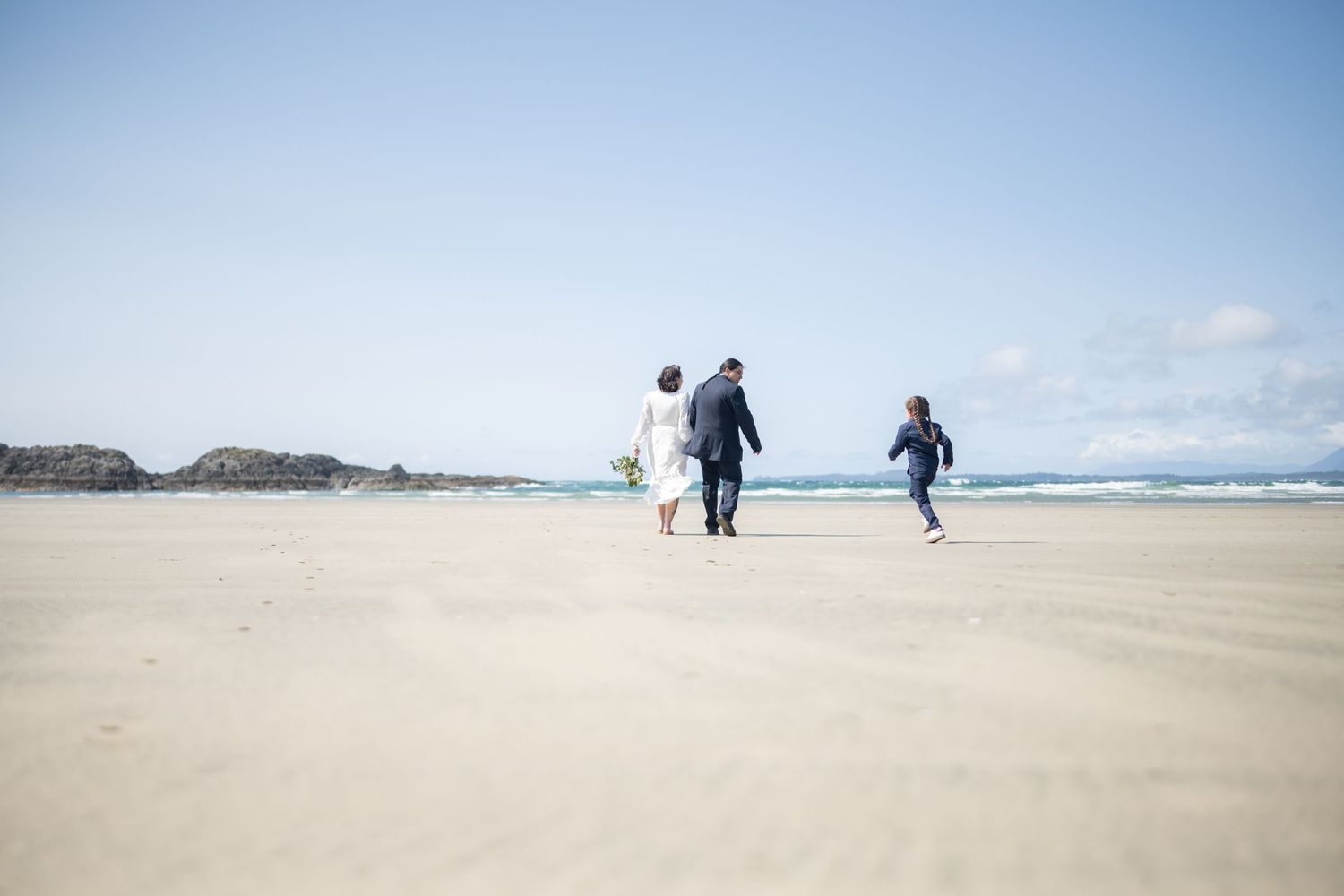 Wide sandy beach with distant figures walking along the shoreline on a bright day.