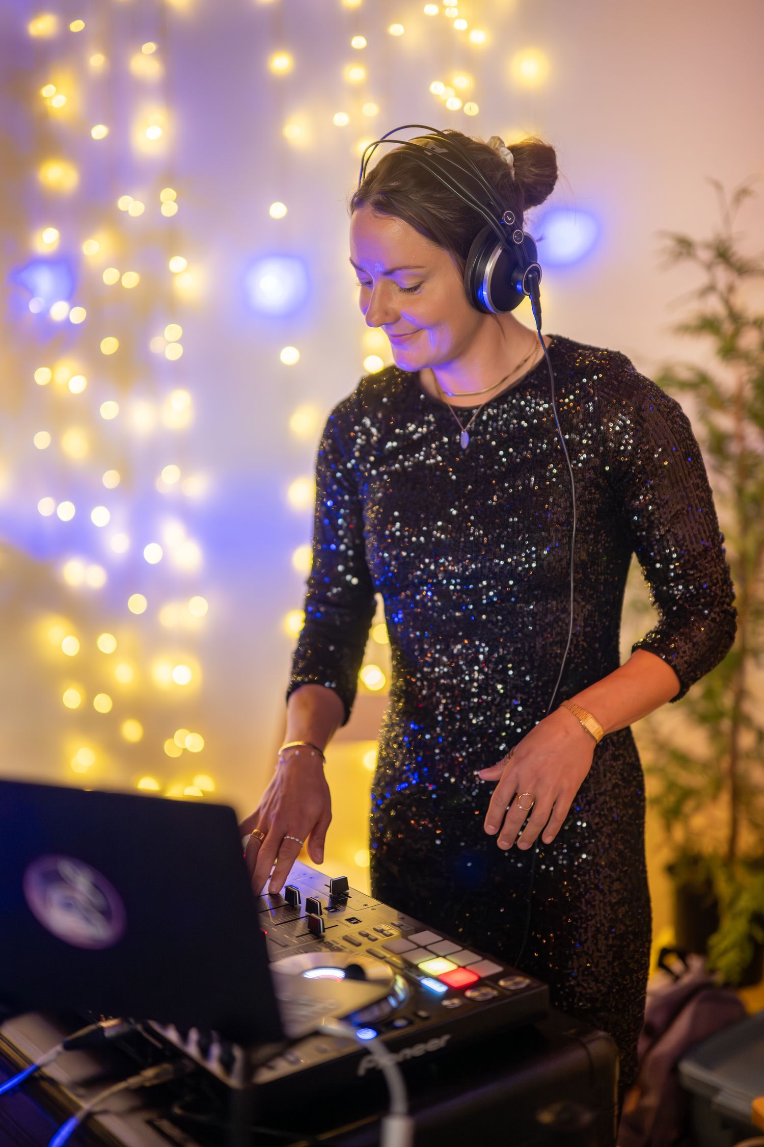 DJ in sparkling attire performing at an event with colorful lighting effects.