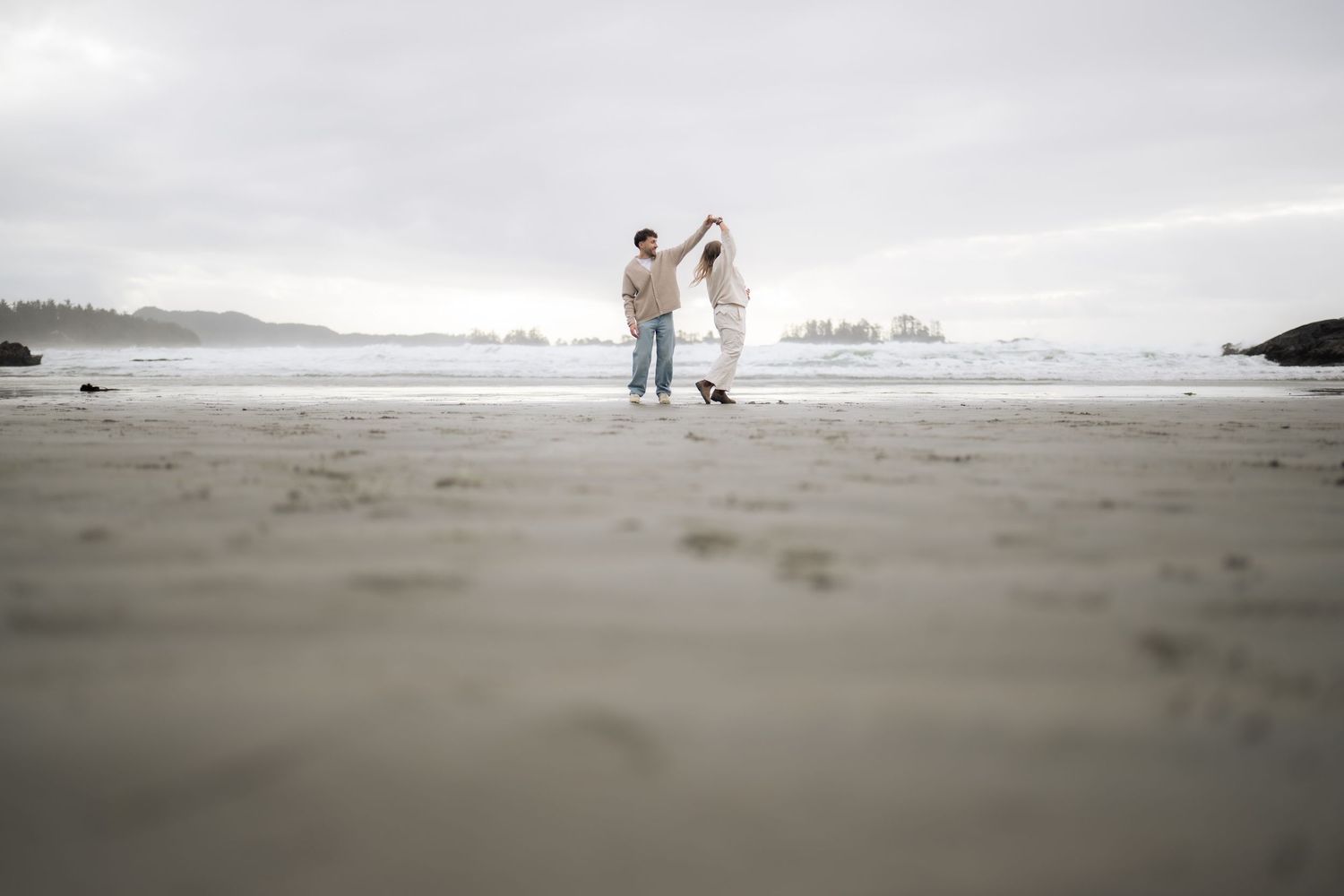 A distant view of two people in light colored outfits walking on a foggy beach.