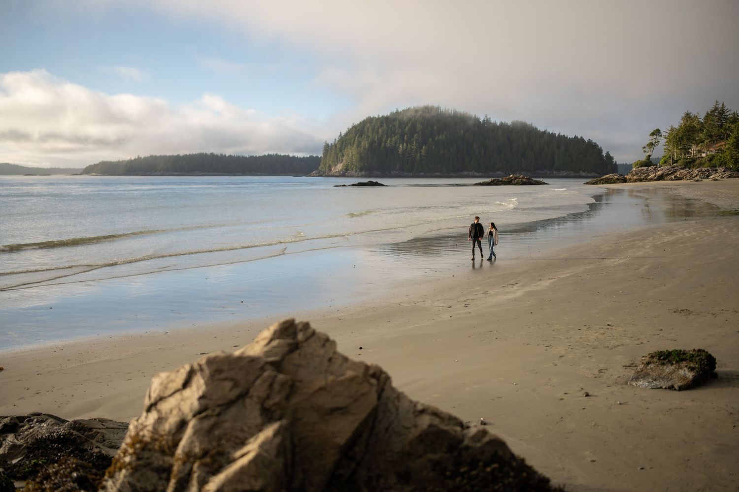 Wide sandy beach with distant cliffs and gentle waves rolling onto shore.