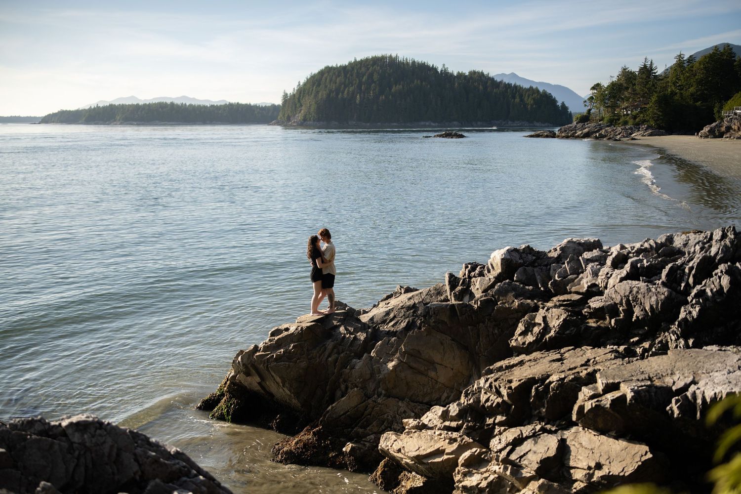 Rocky coastal outcrop overlooking a scenic beach with mountains in the distance.