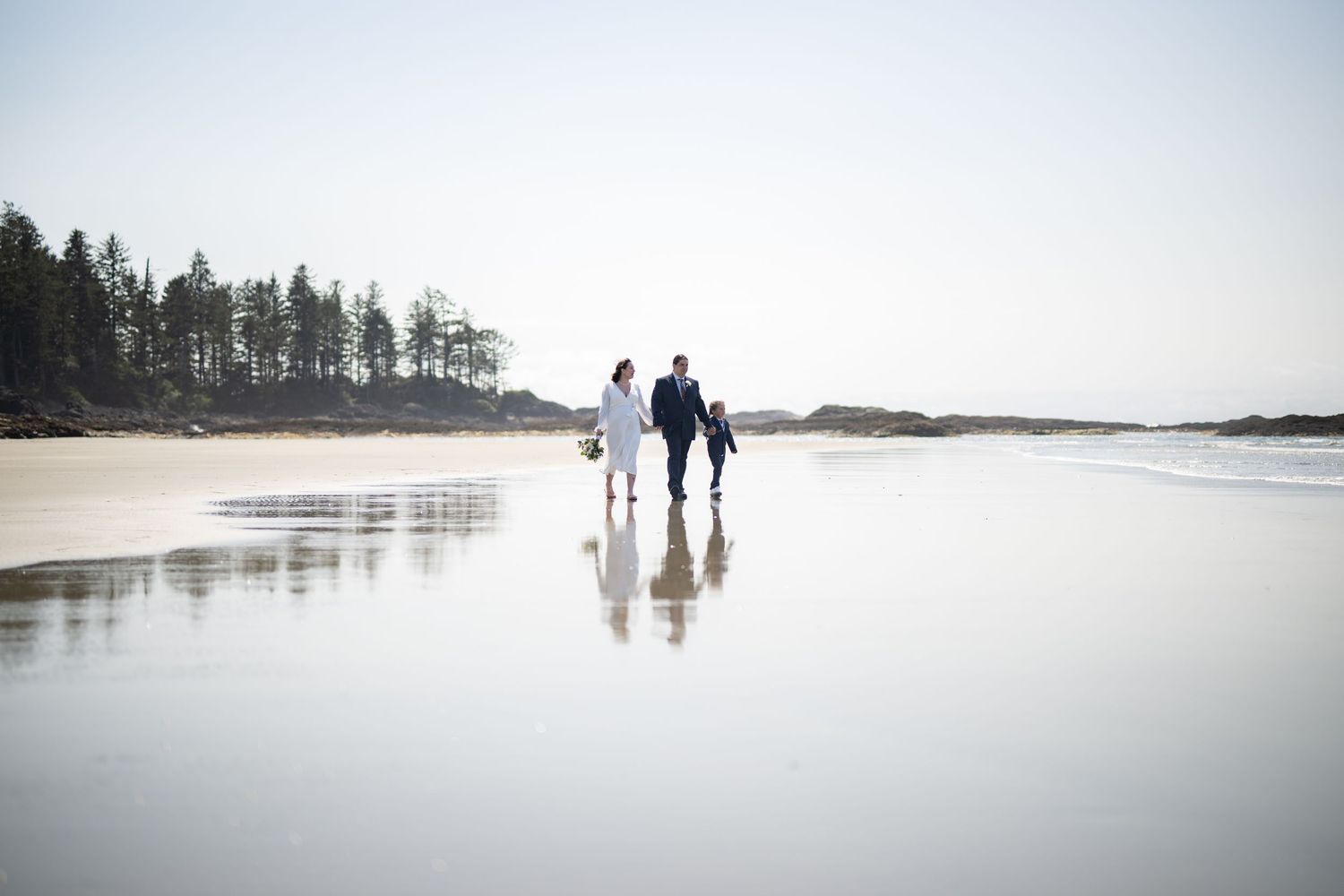 People walking on wide empty beach with forest edge in distance.