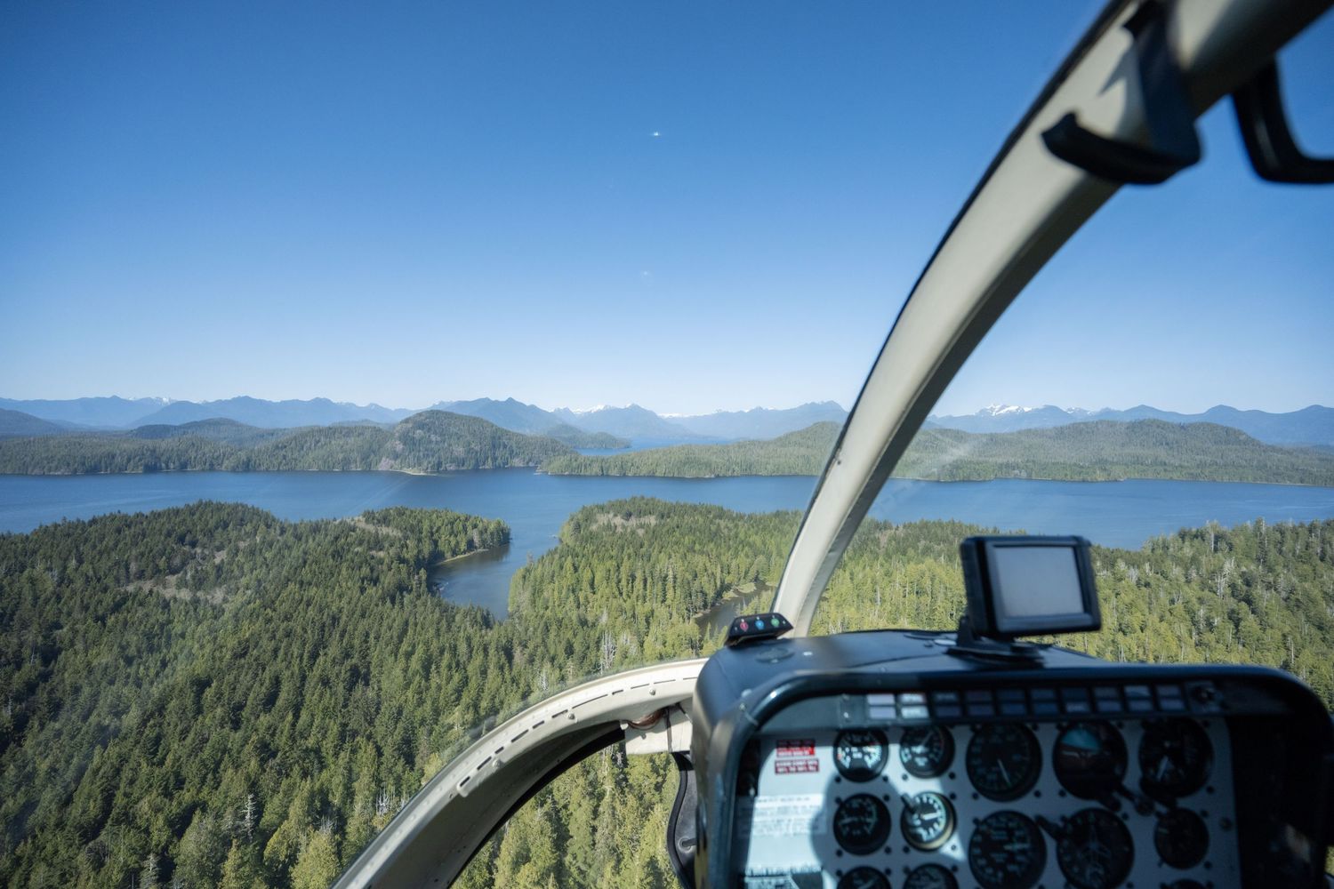 Aerial view of a mountainous landscape with forests and lakes seen through helicopter cockpit windows.