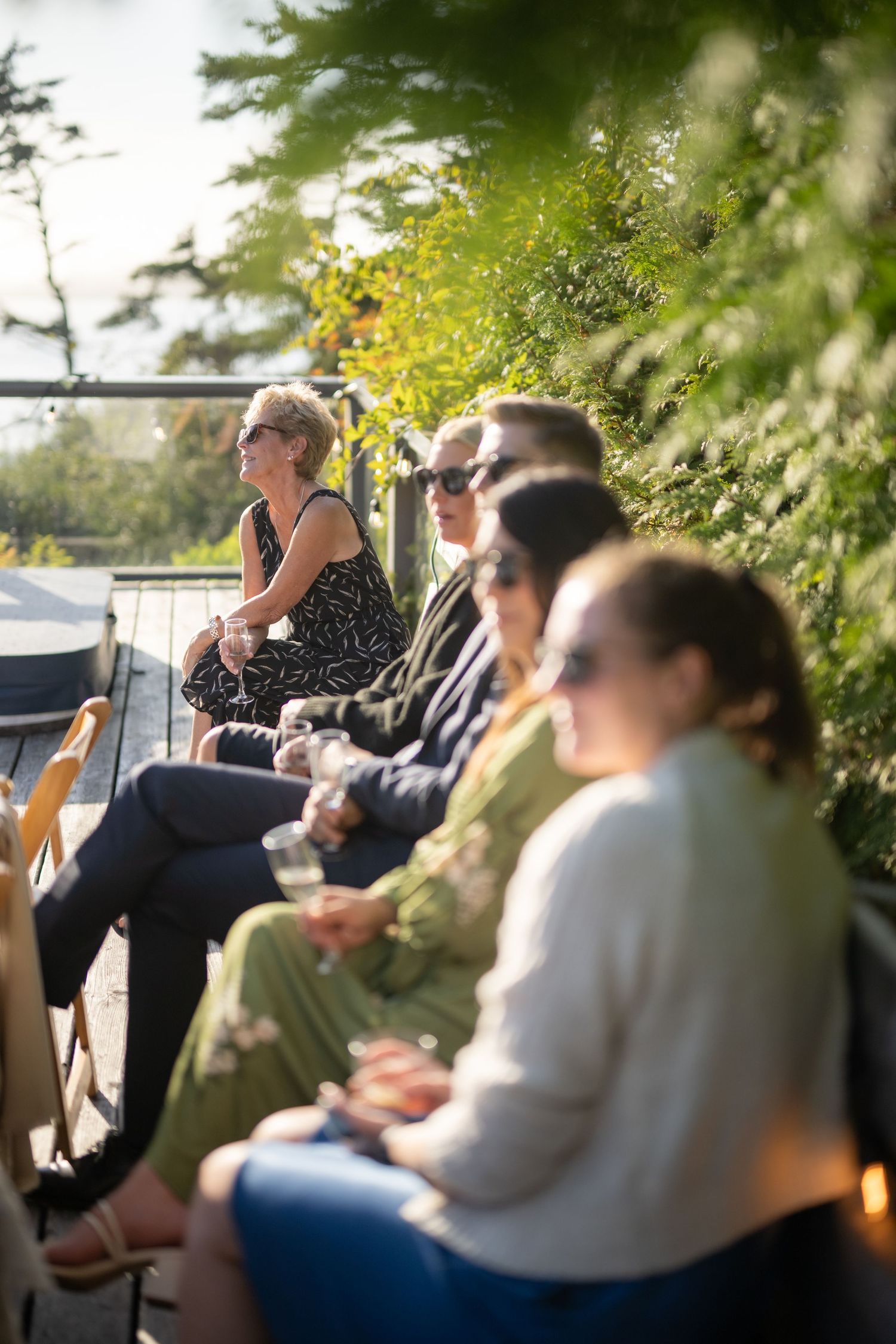 Wedding guests seated outdoors on a sunny day with greenery in the background.
