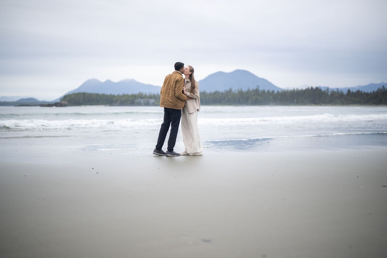 Romantic beach proposal scene with mountains and ocean waves in the background.