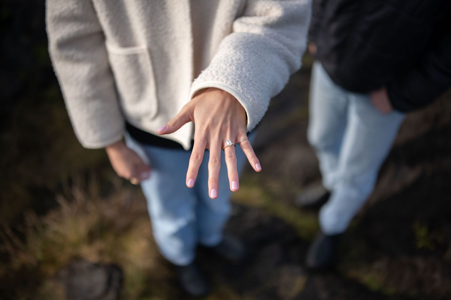 Close-up shot of hands showing an engagement ring on a rocky beach.