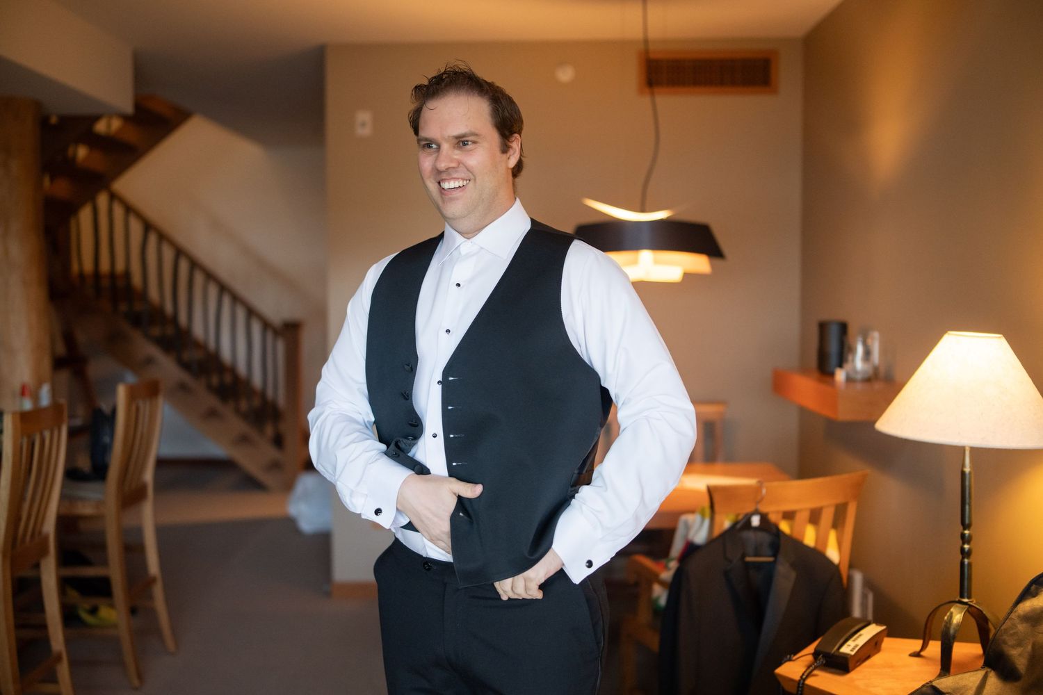 Person adjusting formal attire in a warmly lit room with wooden staircase.