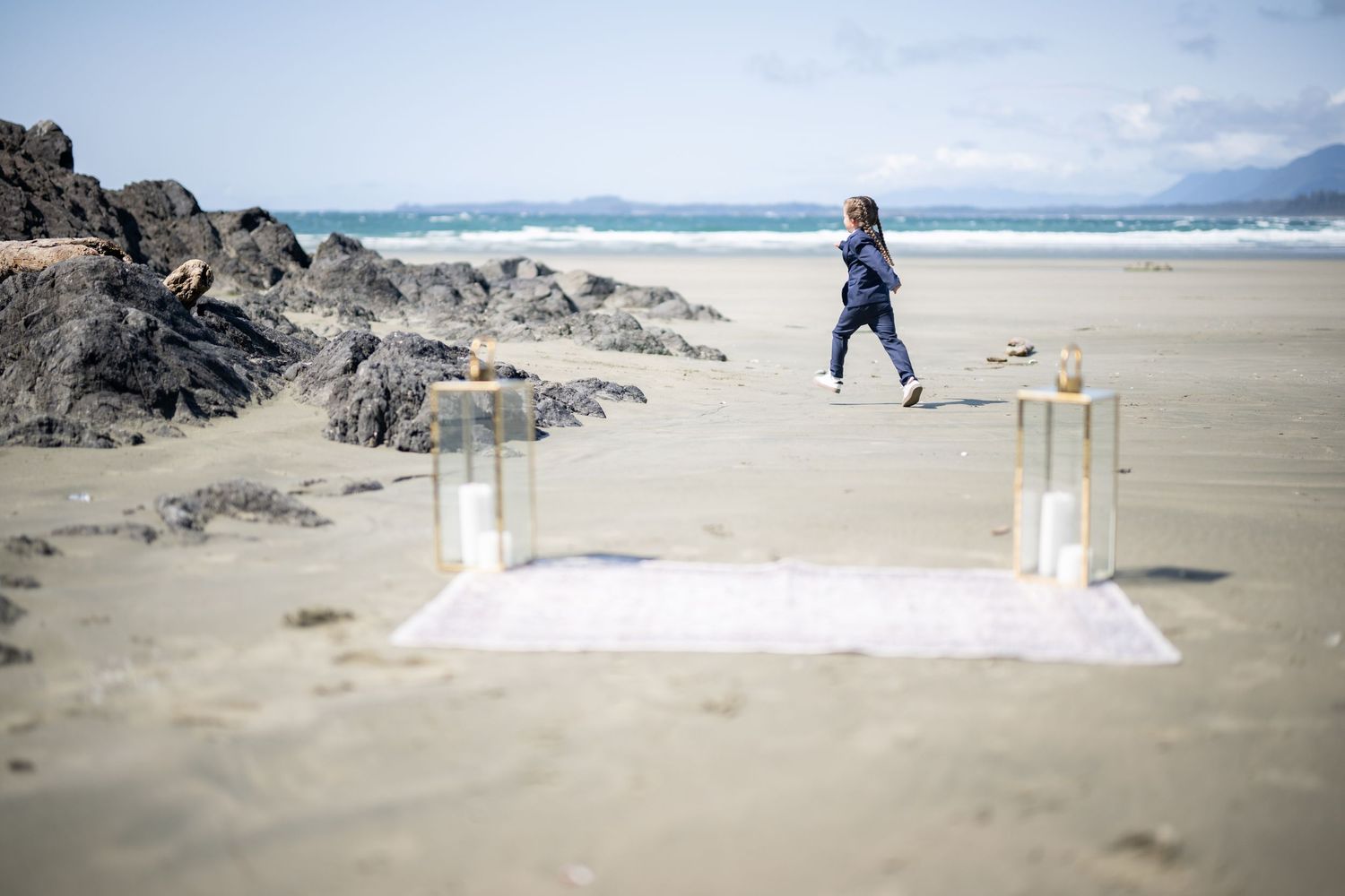 White fabric and pillars set up for a beach ceremony with rocky cliffs in the background.