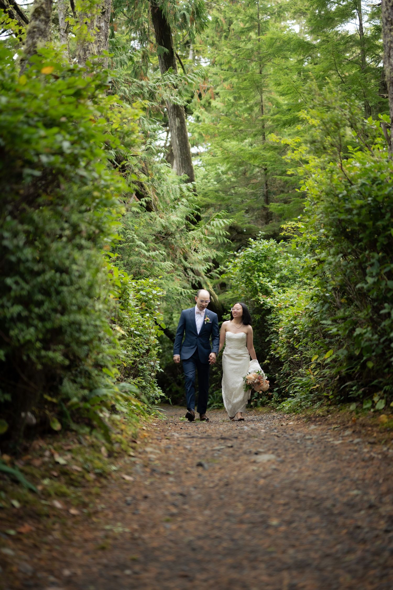 A dirt trail winds through a verdant forest with tall trees and lush greenery.