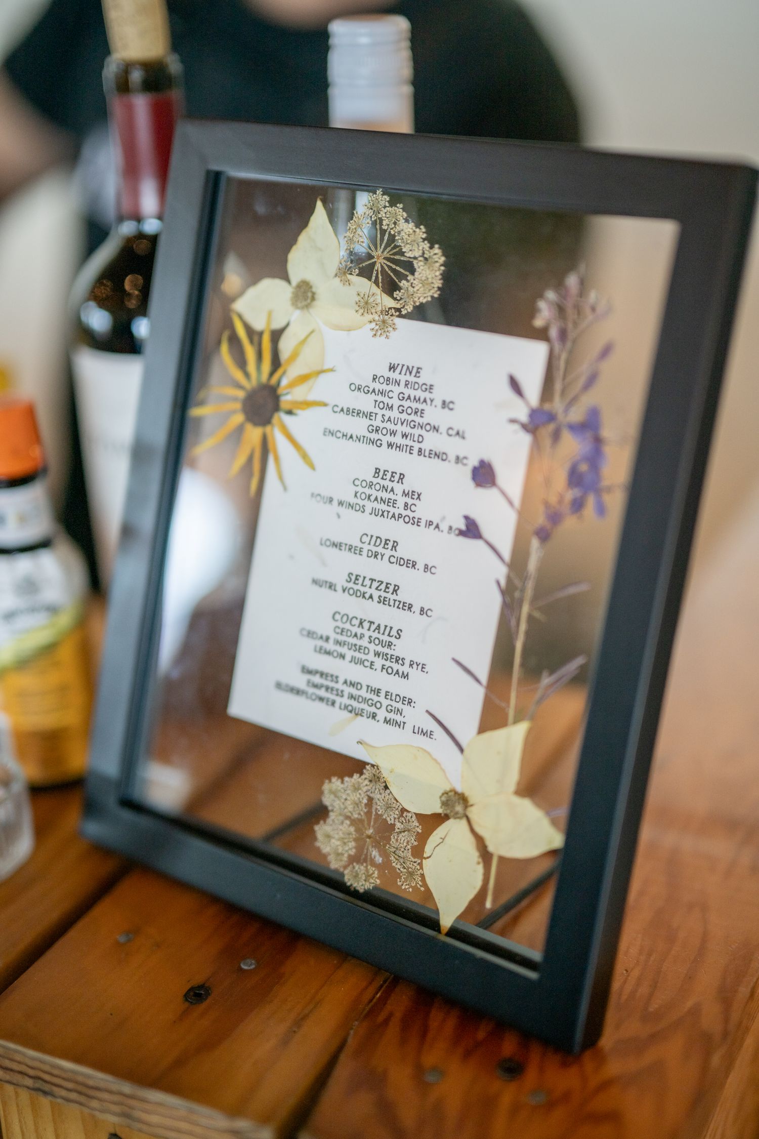 Framed wedding menu cards with delicate floral decorations displayed on wooden surface.