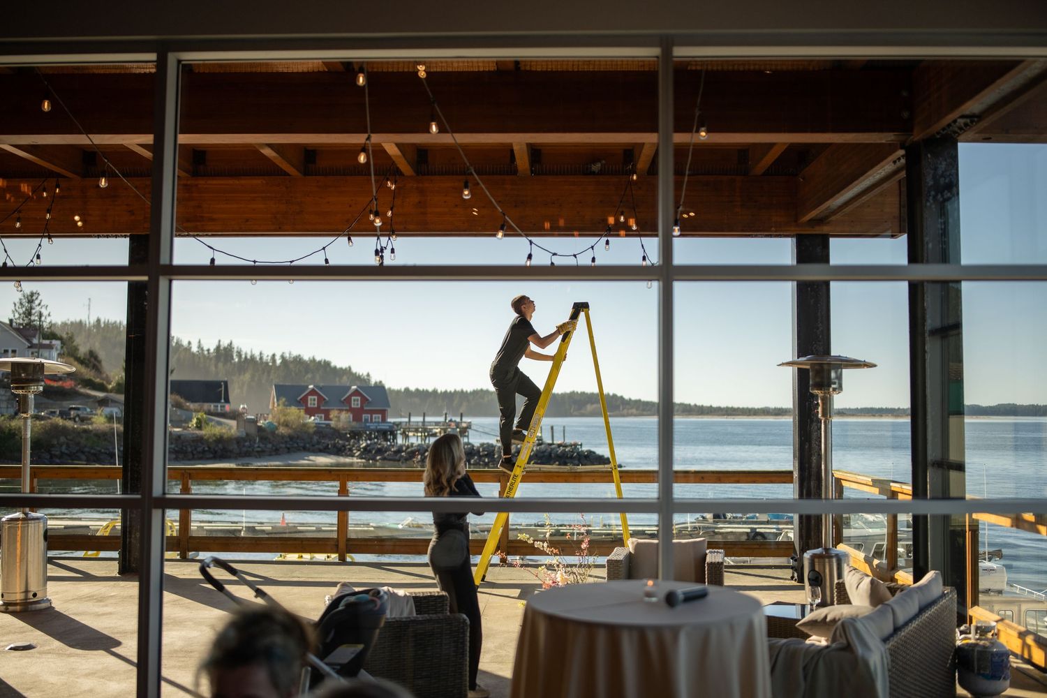 Silhouette of worker setting up event space with stunning waterfront views through large windows.