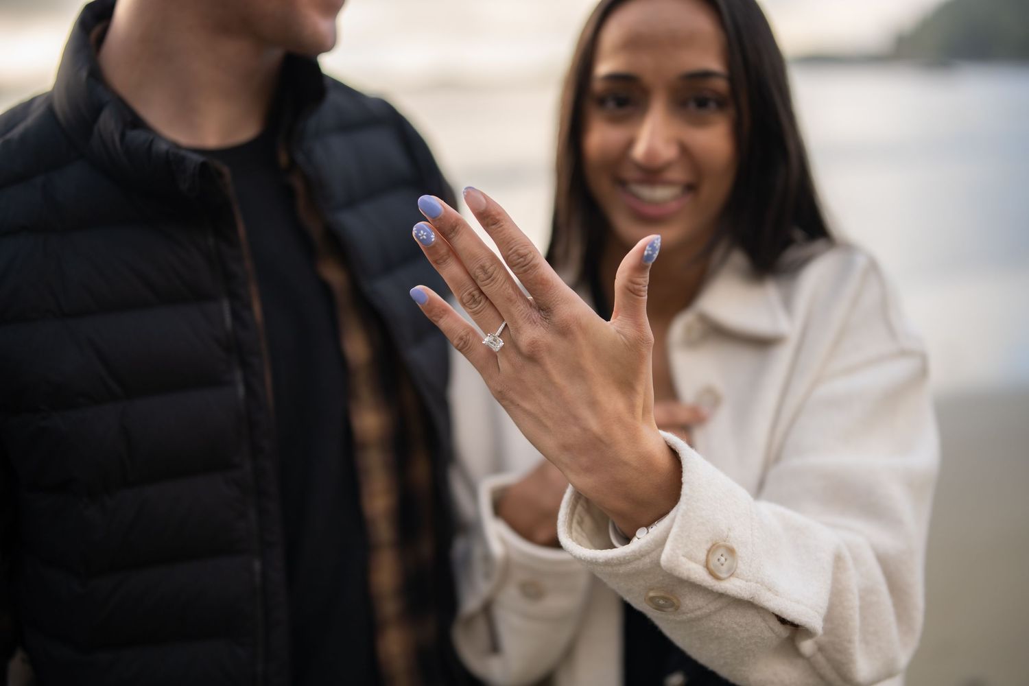 Close up of a hand showing off a new engagement ring on a cloudy day.