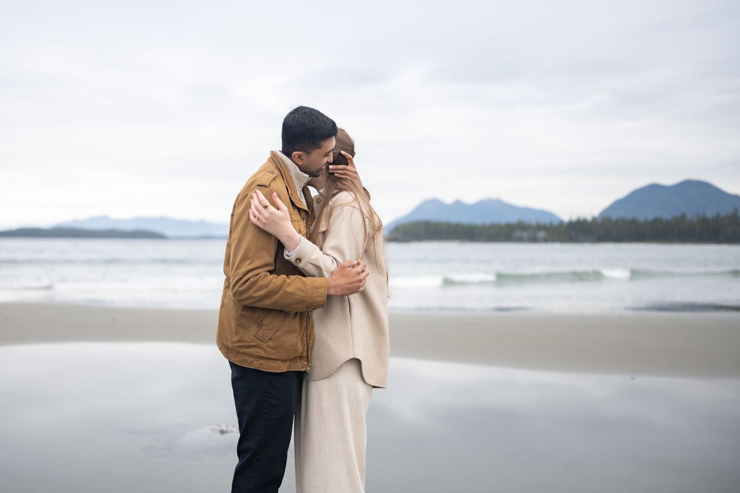 Romantic beach photoshoot with mountains and cloudy skies in the background.