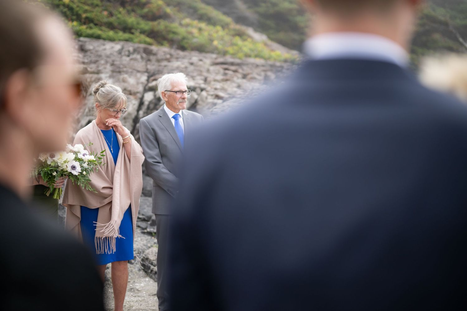 Small group of wedding attendees stand together on a misty coastal beach.