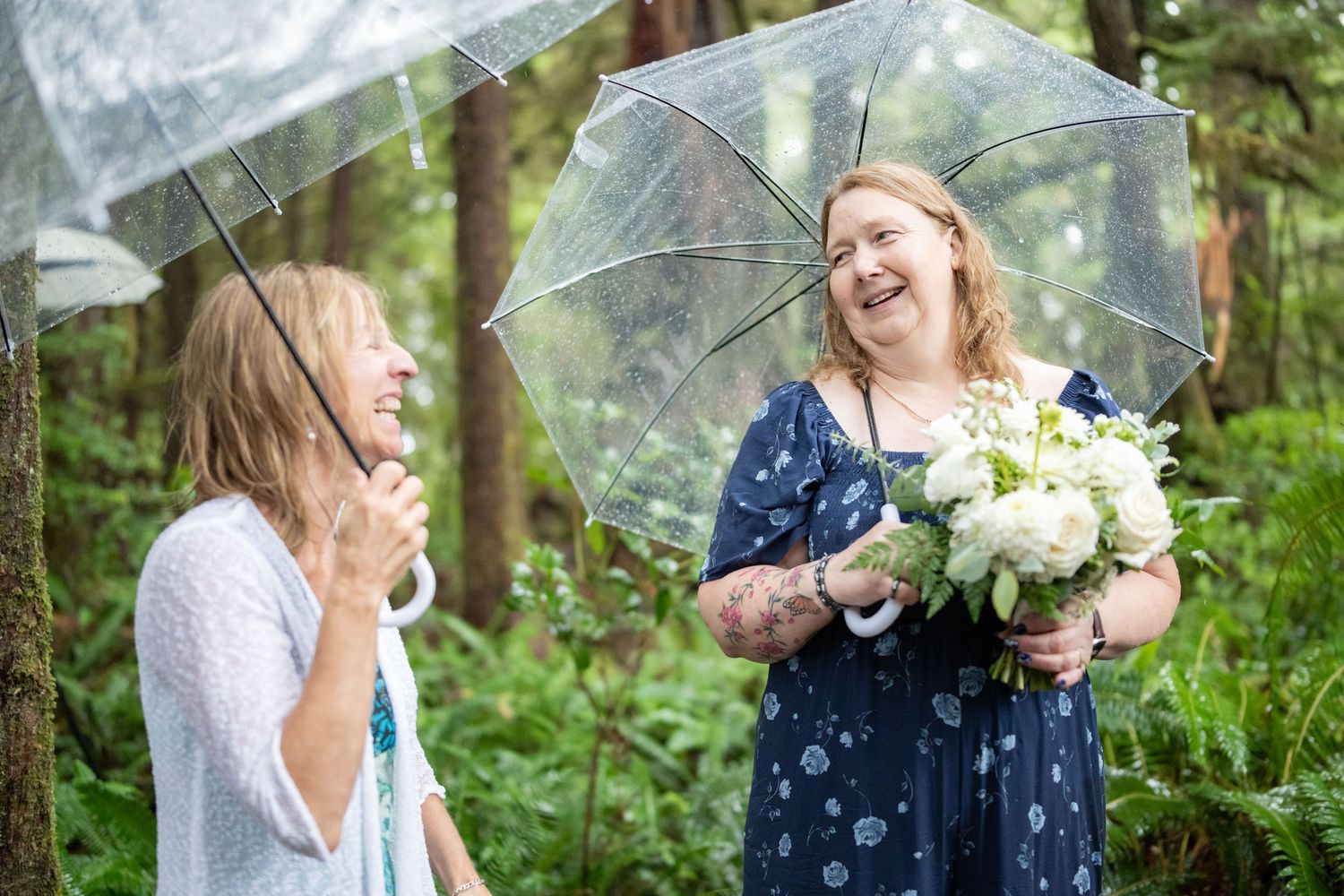 Wedding guests smile and celebrate under clear umbrellas in a forest.