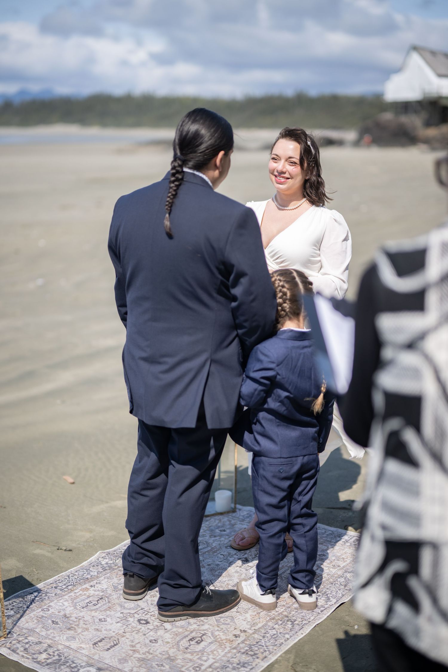 A white patterned blanket laid out on the beach sand during a seaside ceremony.