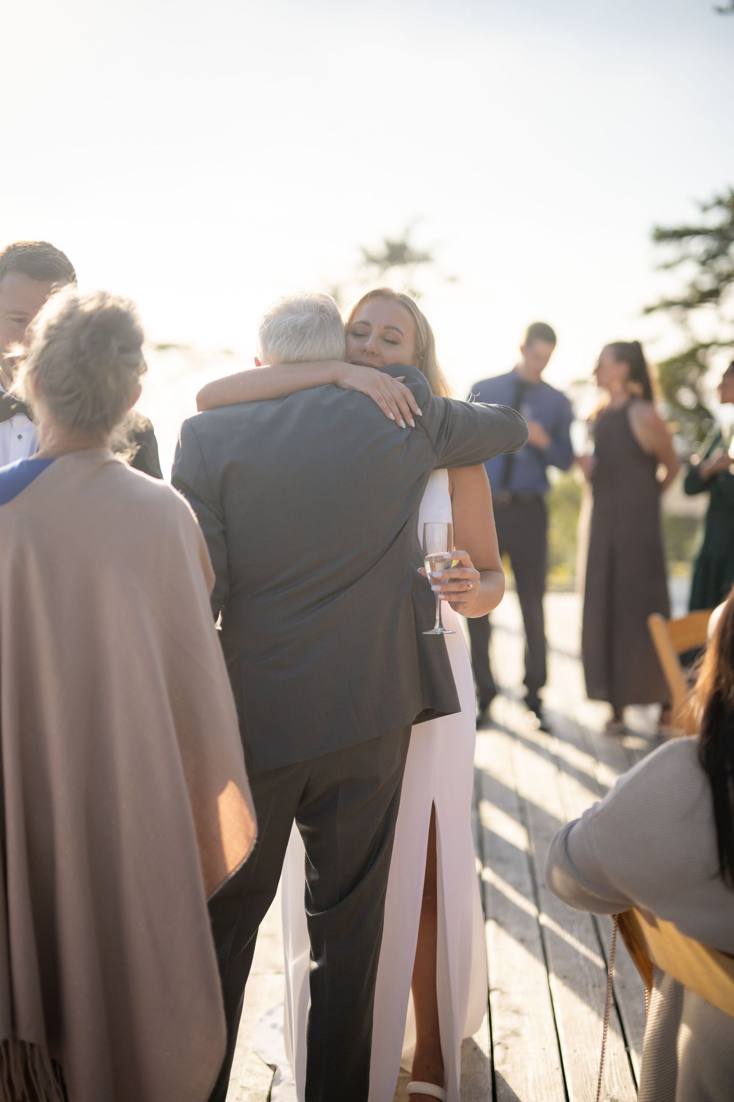 Emotional moment at an outdoor wedding reception with guests embracing in golden sunlight.