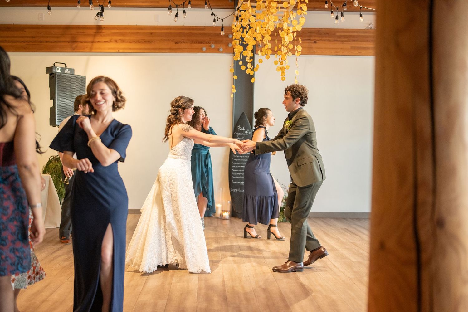 People dancing and enjoying themselves at a wedding reception in a rustic venue with overhead lighting.