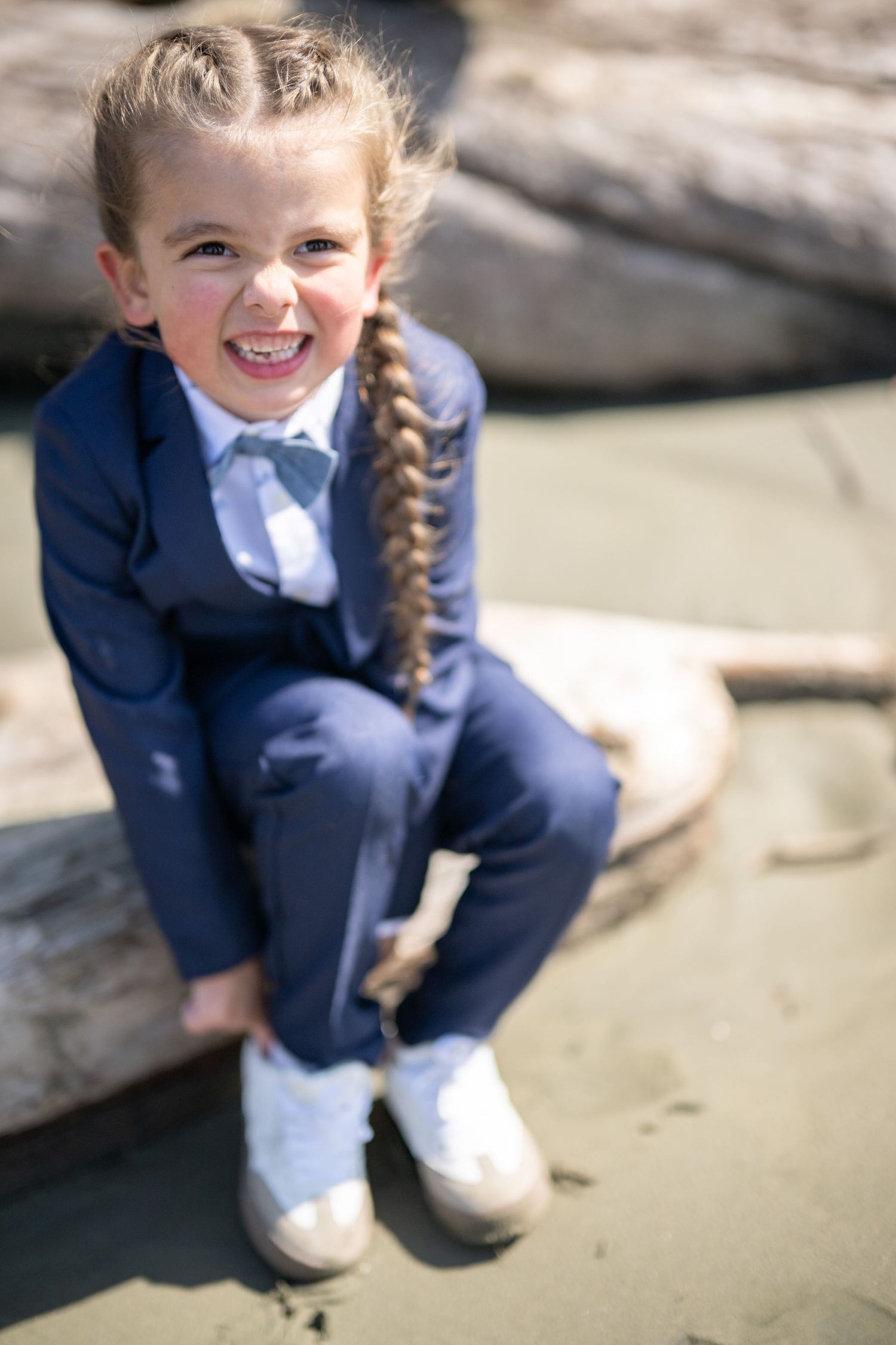 Child in navy blue outfit crouches playfully on sandy beach.