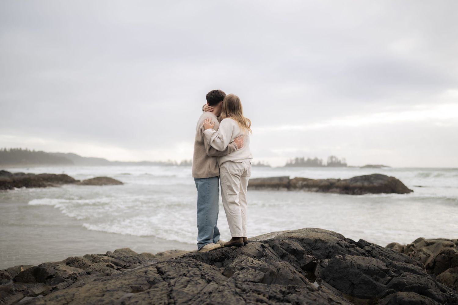 A couple sharing an intimate moment while standing on rocky coastal cliffs overlooking the ocean.