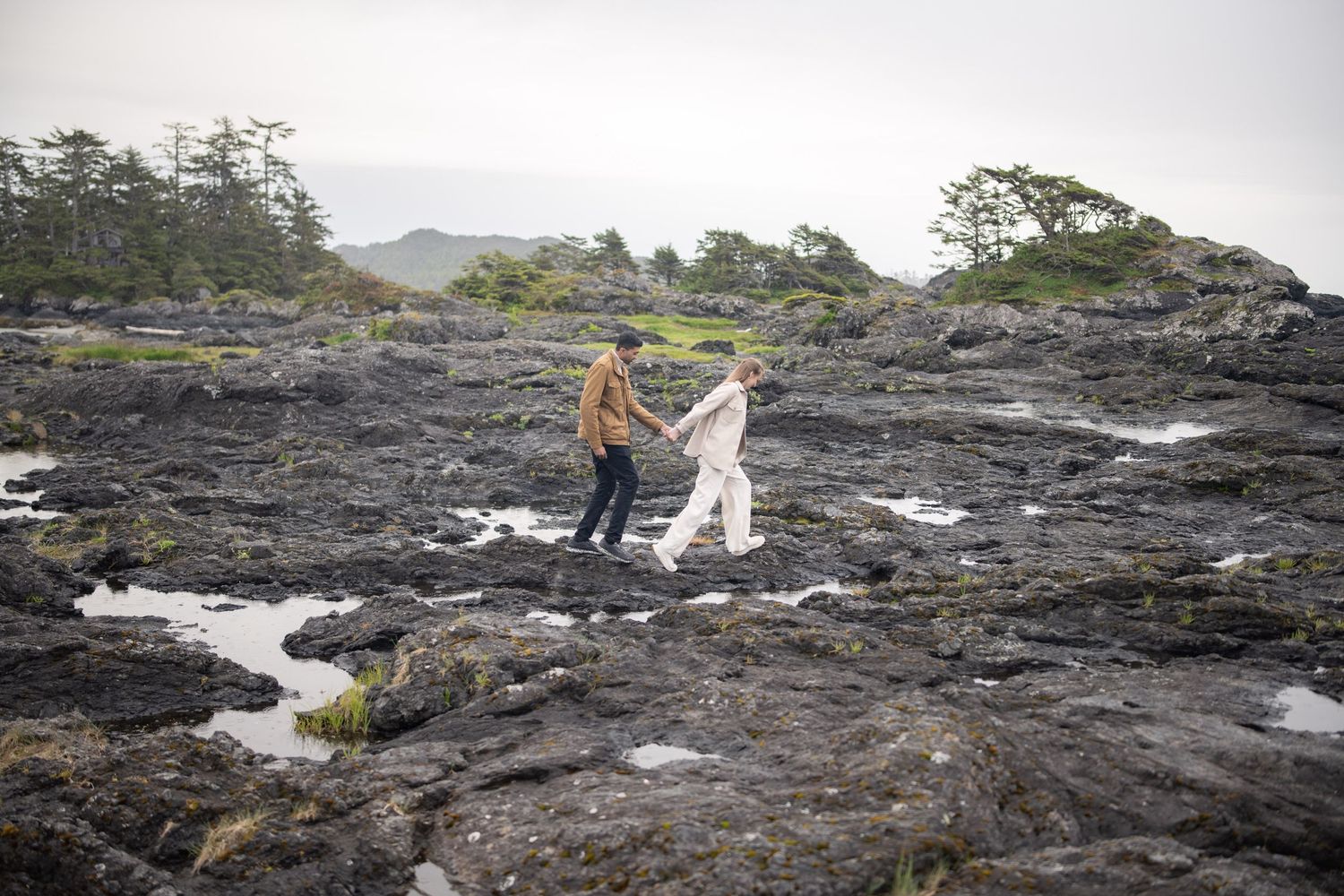 Dramatic rocky coastline with waves crashing against dark volcanic rocks on an overcast day.