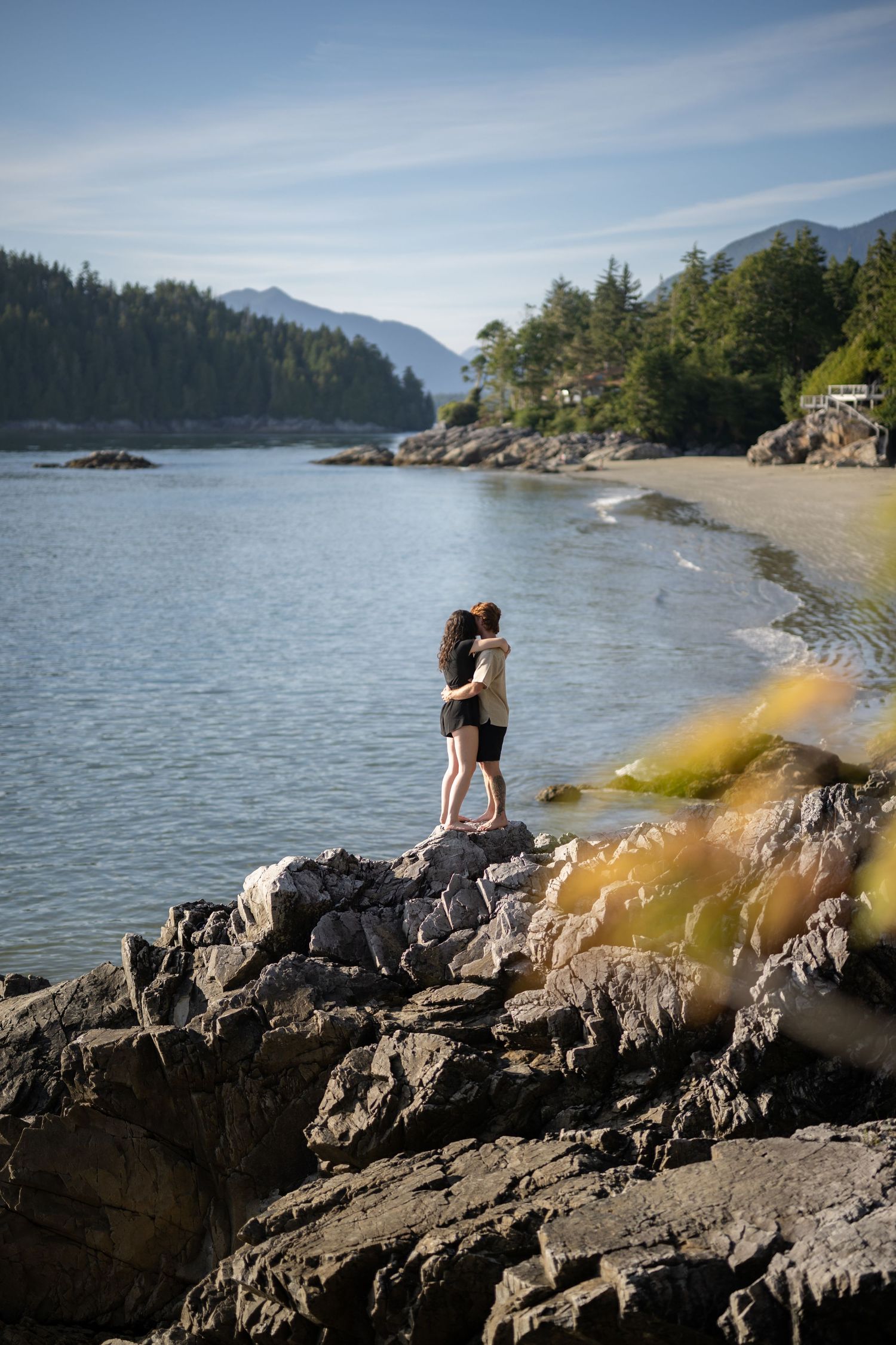 Silhouettes against a bright sky on rugged coastal rocks with ocean and forest views.