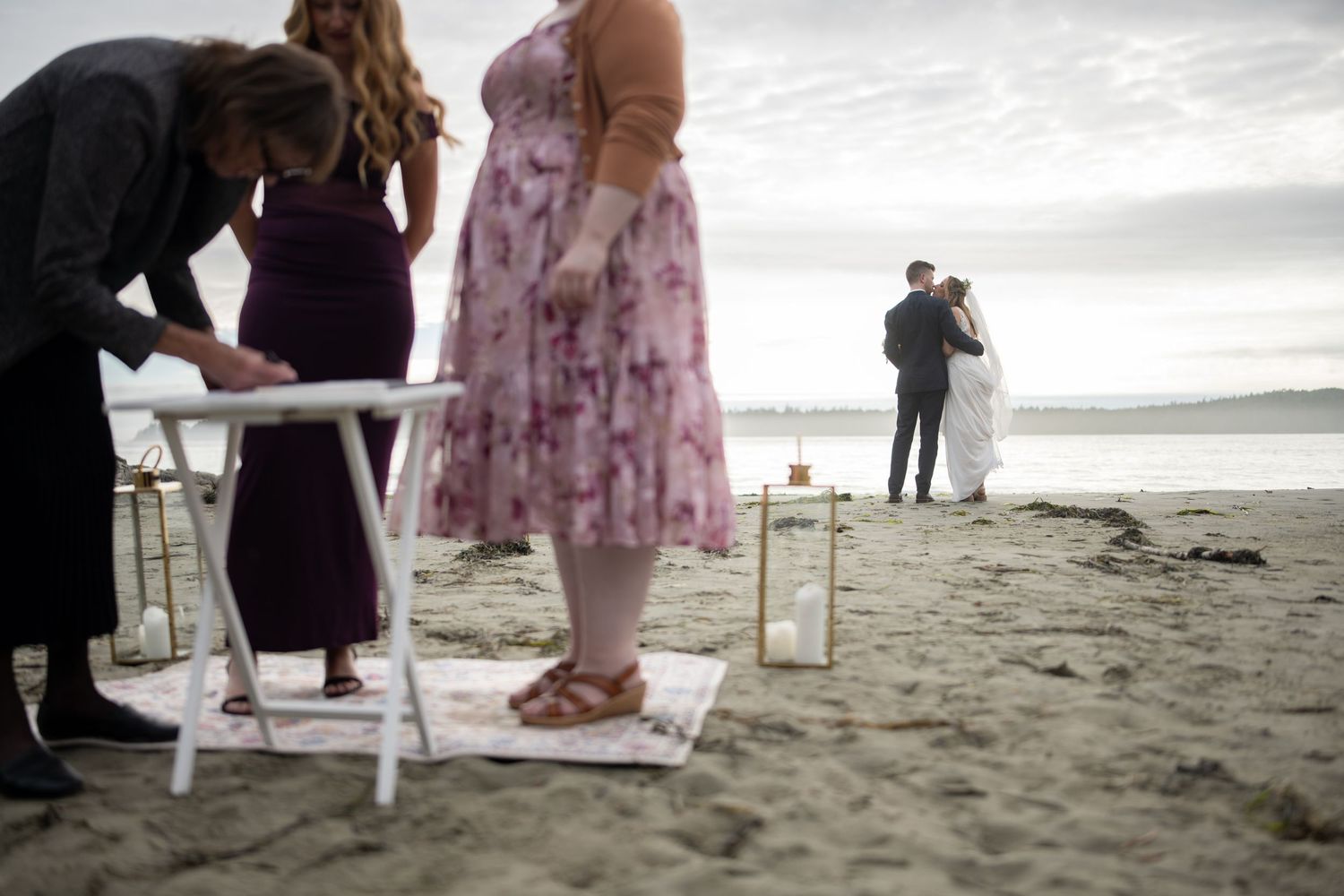 Wedding party in floral dresses and formal attire on sandy beach.