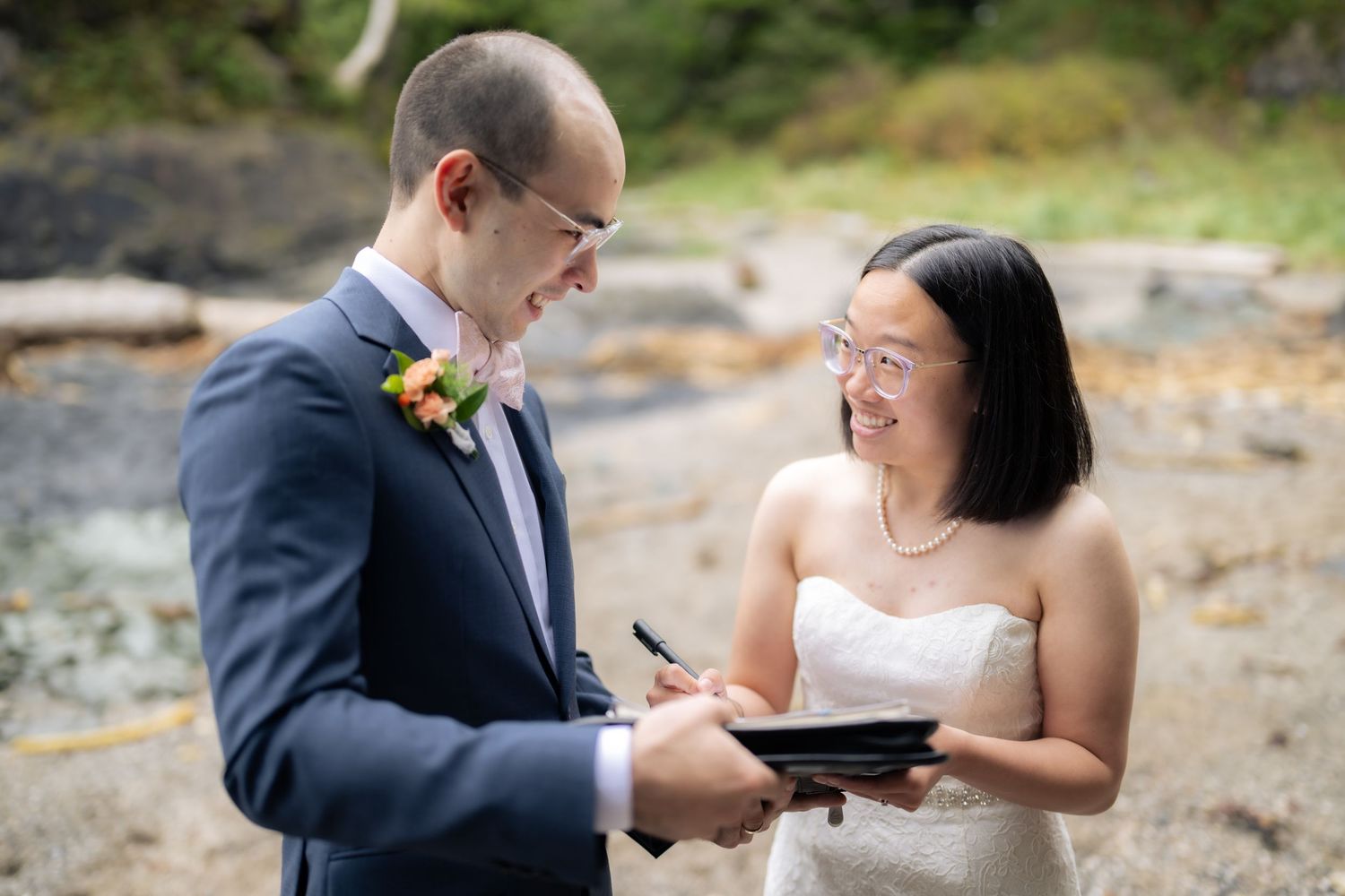 Two people exchange smiles and laughter while reading their vows on a scenic coastal backdrop.