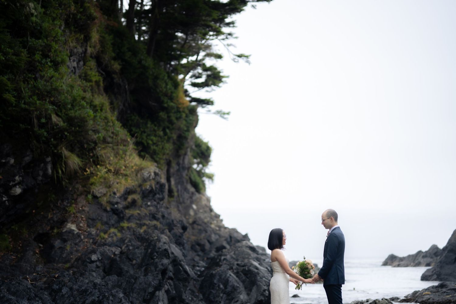 Wedding ceremony taking place on a secluded Pacific Northwest beach with dramatic rocky cliffs.
