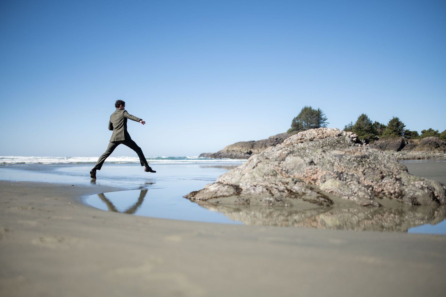 A silhouette leaps gracefully across wet sand on a scenic beach with rocky cliffs.