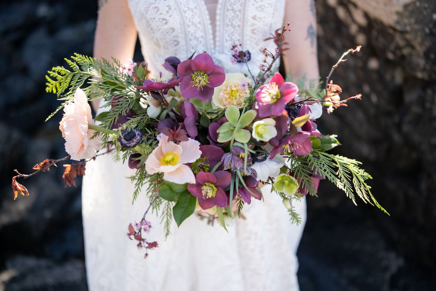 Colorful wedding bouquet featuring purple orchids and mixed flowers against white lace.