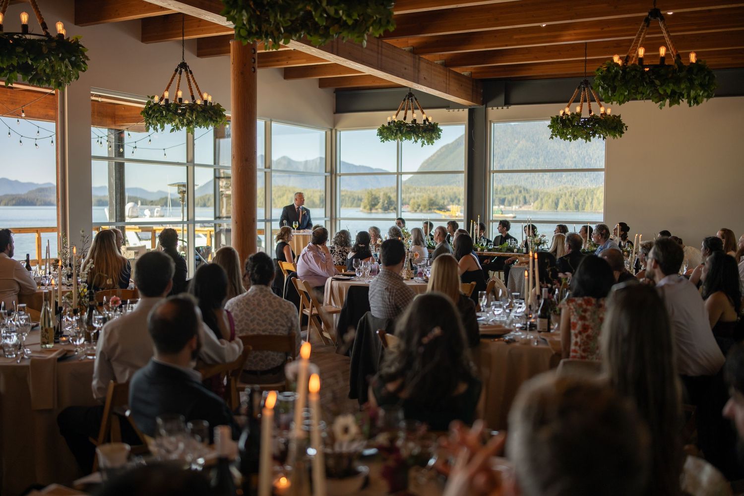 Spacious reception venue with panoramic water views and guests seated at round tables.