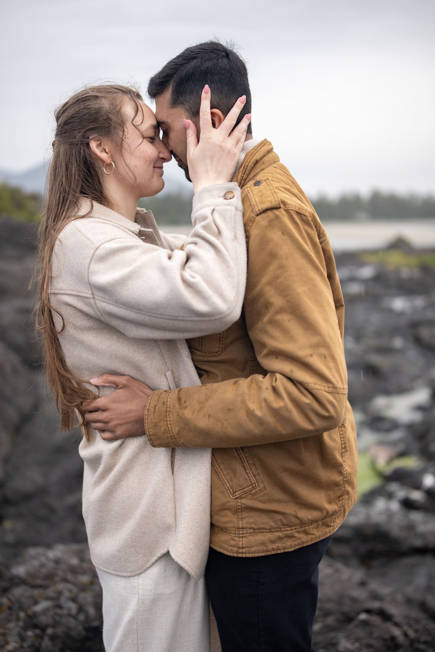 Two people share an intimate moment on dark rocky coastal terrain.