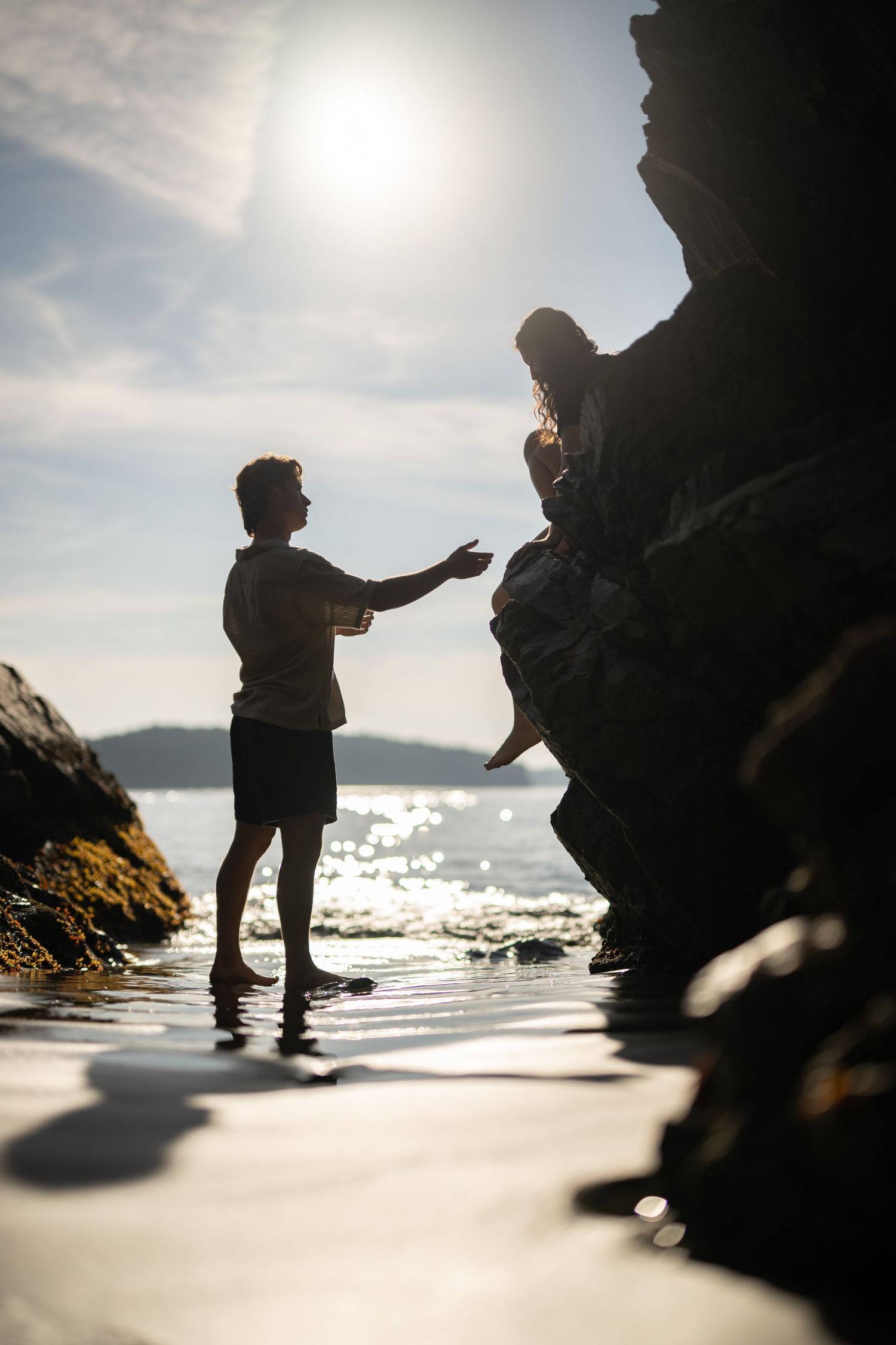 Dramatic silhouettes against bright sunlight on a rocky beach with sparkling water.